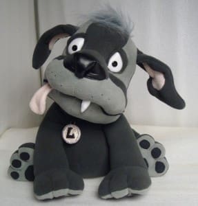 Lou the dog plush sewn from an illustrator's drawing, tongue out and an L medallion