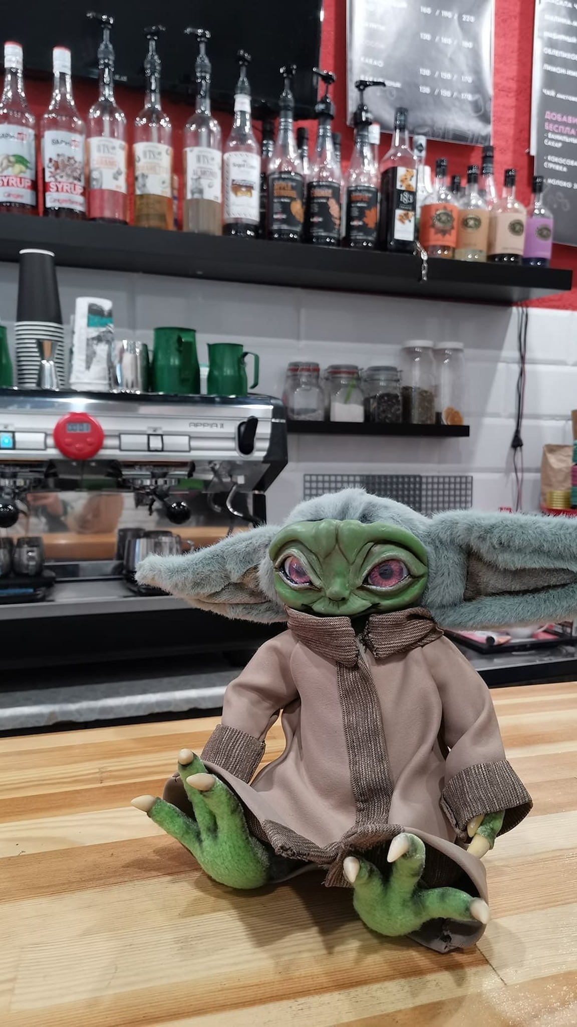 Custom Baby Yoda doll sitting on a wooden counter in a cafe, a handmade Grogu doll about 10 inches tall
