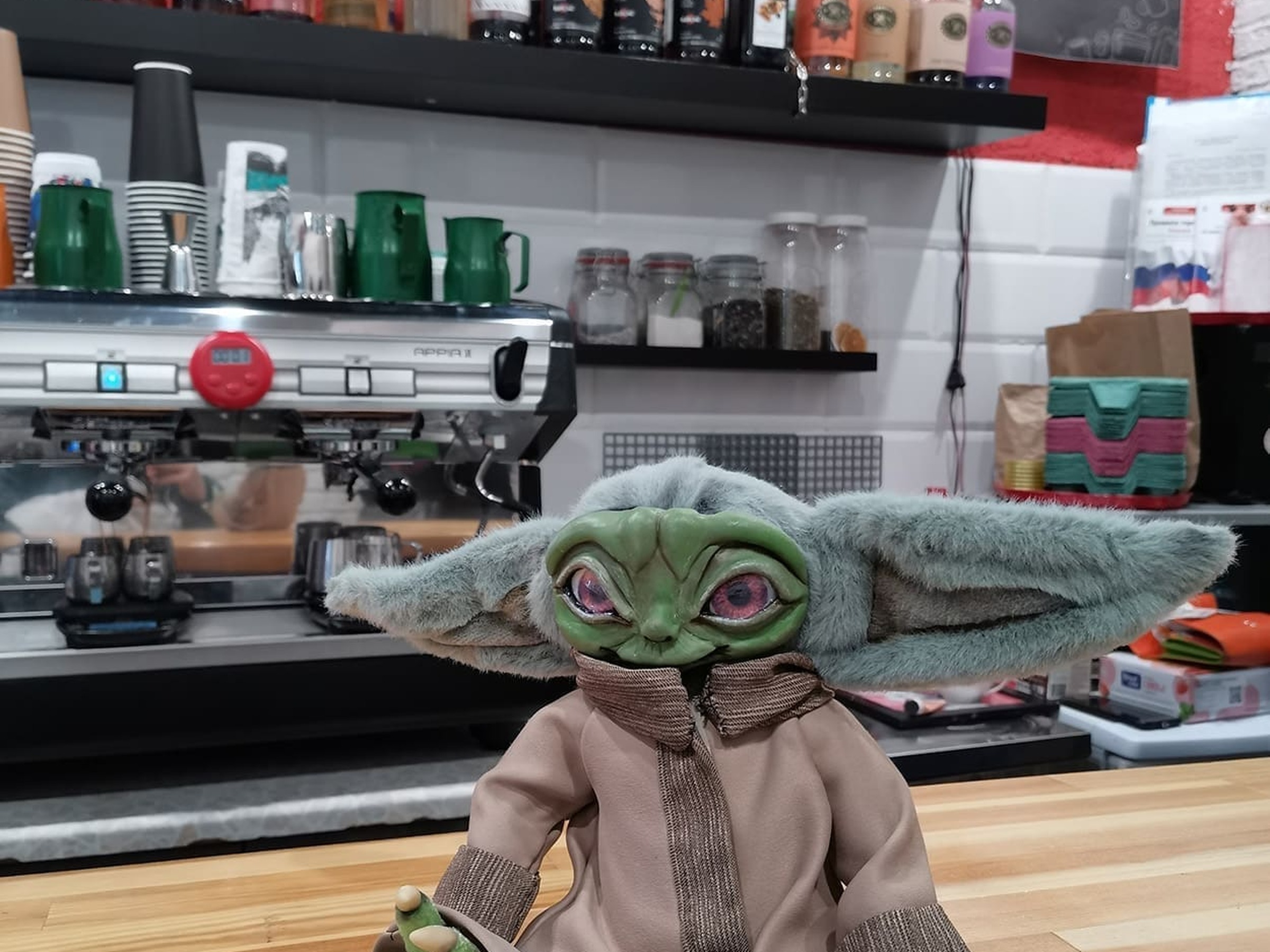 Baby Yoda Doll in a Cafe, Handmade Grogu Custom Baby Yoda doll sitting on a wooden counter in a cafe, a handmade Grogu doll about 10 inches tall