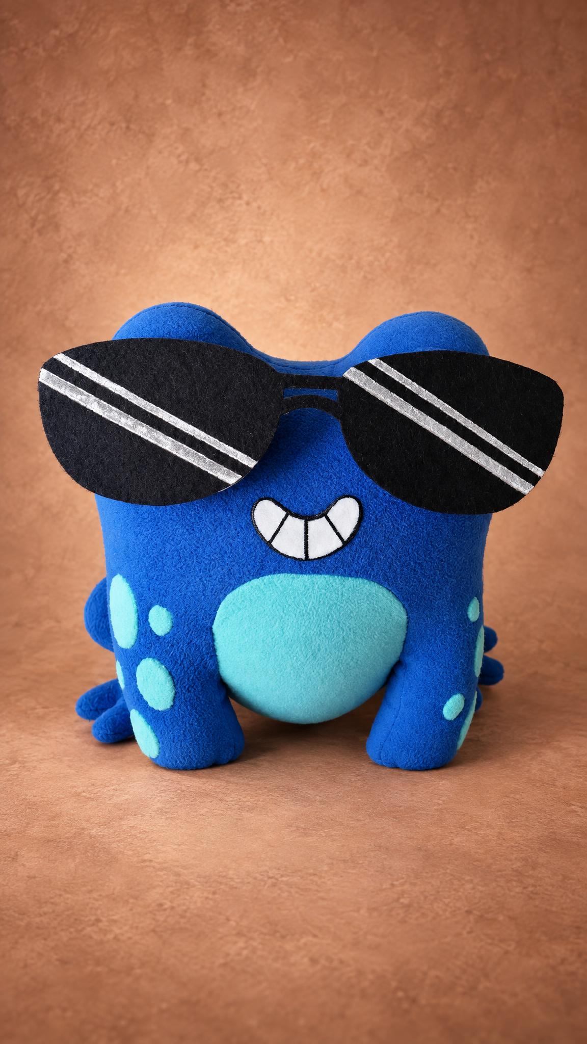 Handmade blue frog plush with striped sunglasses and a grin, a custom toy from a drawing