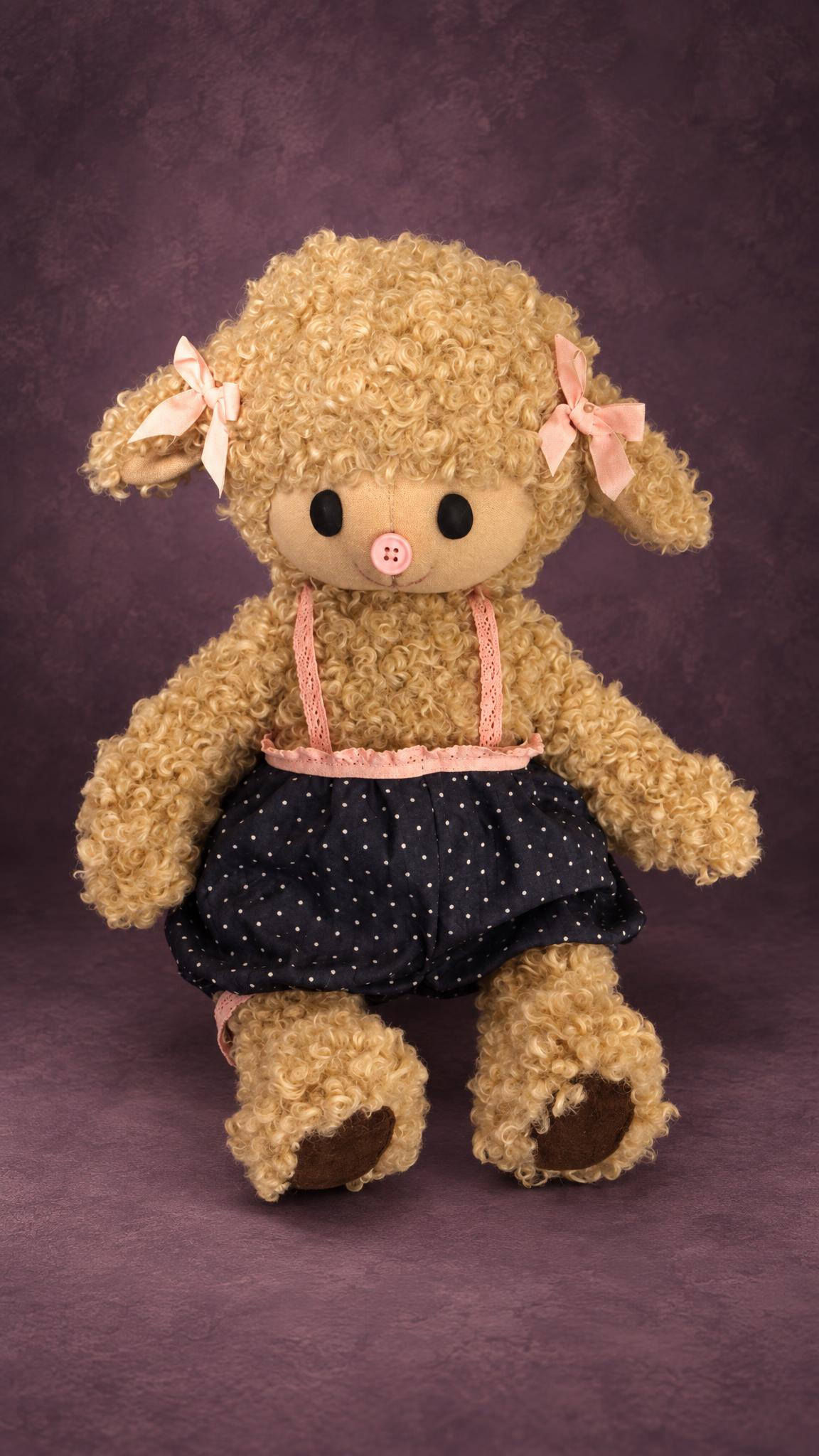 Curly sheep plush in a navy polka-dot skirt with pink lace braces, a handmade prototype for a toy brand