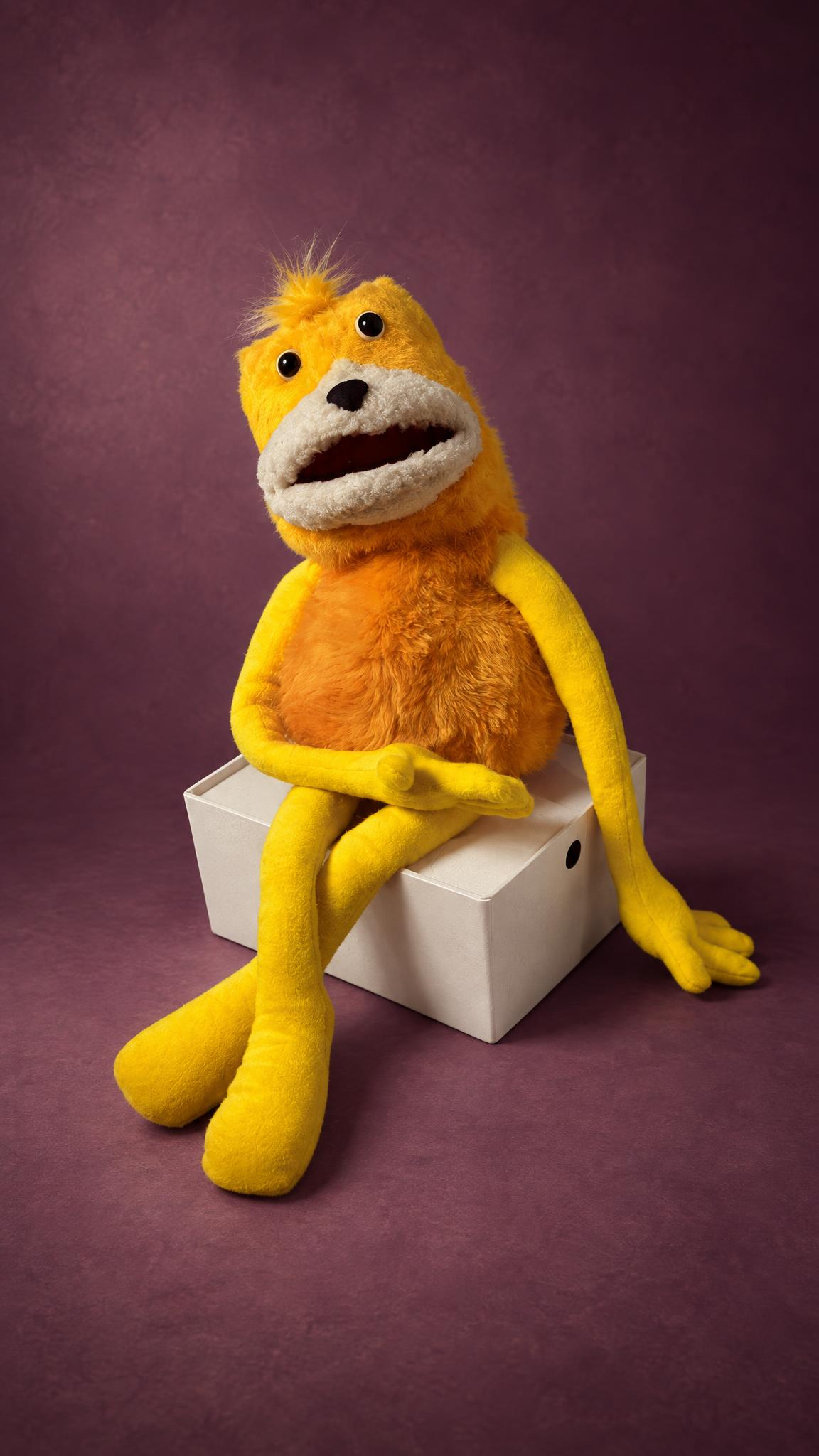 Handmade Flat Eric puppet made to order, yellow fur, long floppy arms, sitting on a white box