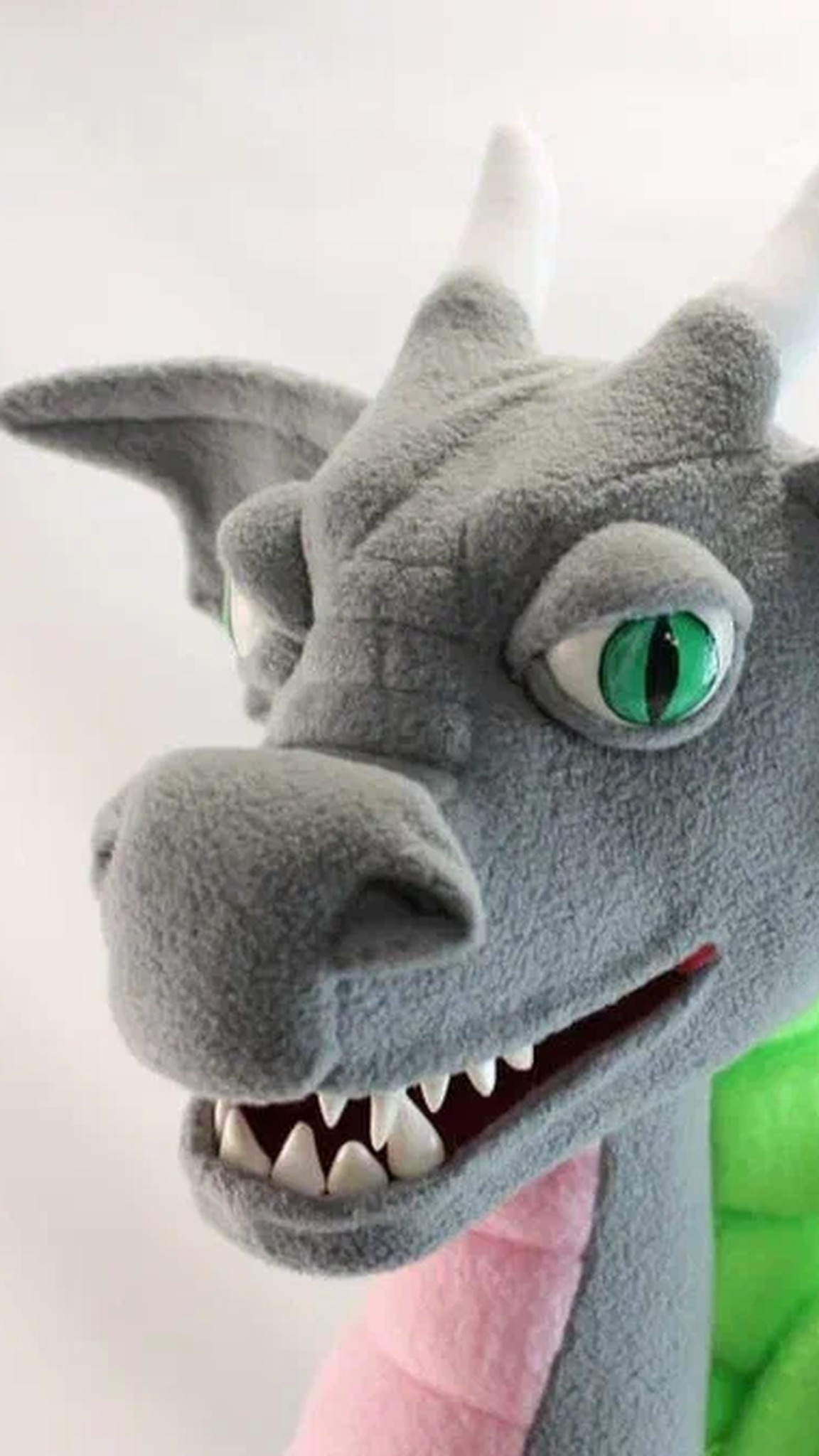 Gray dragon plush head with green slit eyes, white horns and a toothy grin, a custom esports mascot sewn by hand