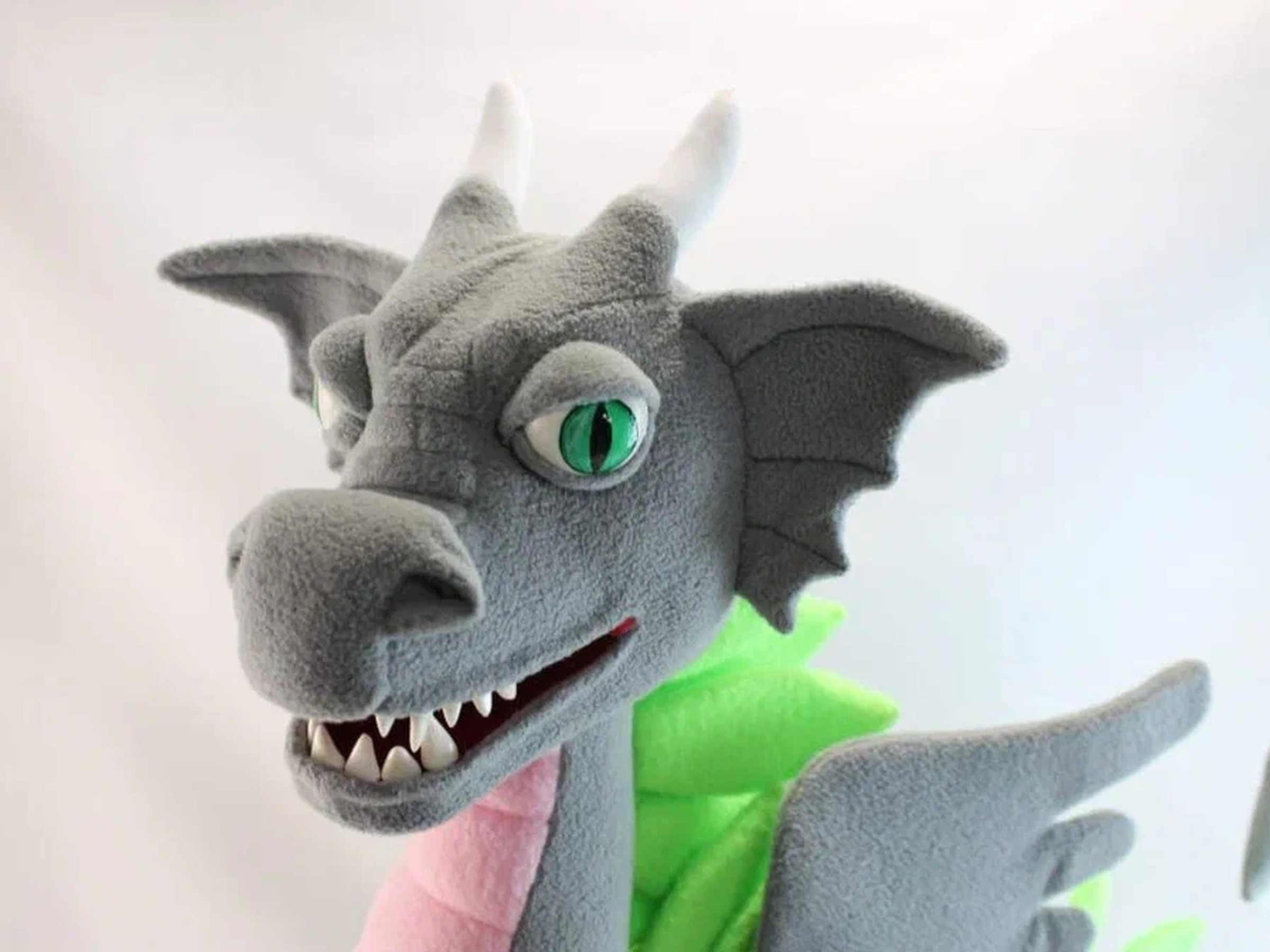 Gray dragon plush with green eyes and white horns Gray dragon plush head with green slit eyes, white horns and a toothy grin, a custom esports mascot sewn by hand