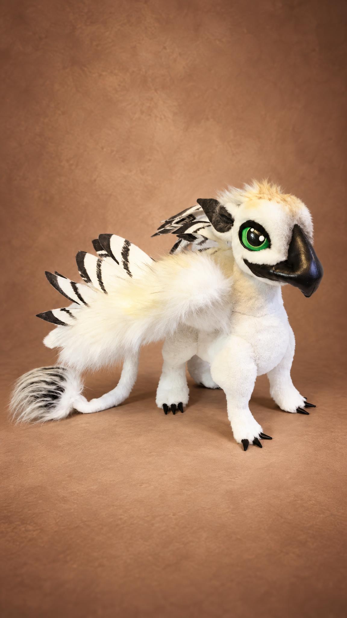 Custom griffin stuffed animal in white fur with black-tipped wings and green eyes, sewn to order from a drawing