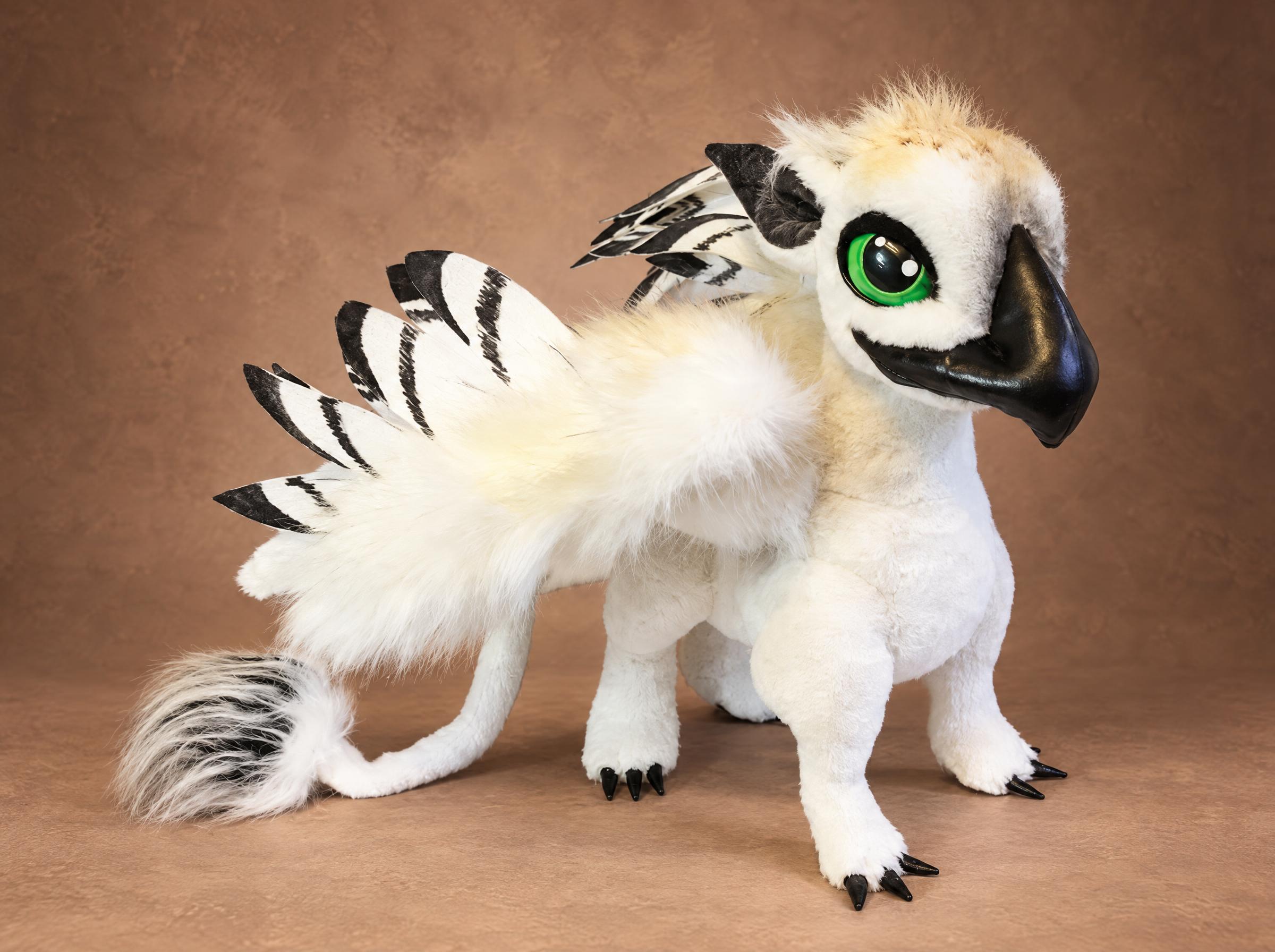 White griffin plush with green eyes, a black beak and black-tipped feathered wings, a custom mythical creature made to order