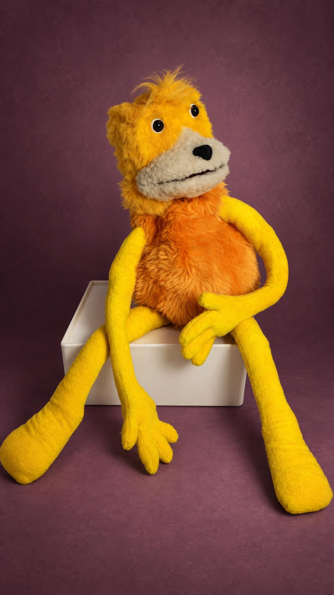 Handmade Flat Eric plush puppet made to order, yellow fur, cream muzzle, long legs dangling from a white box