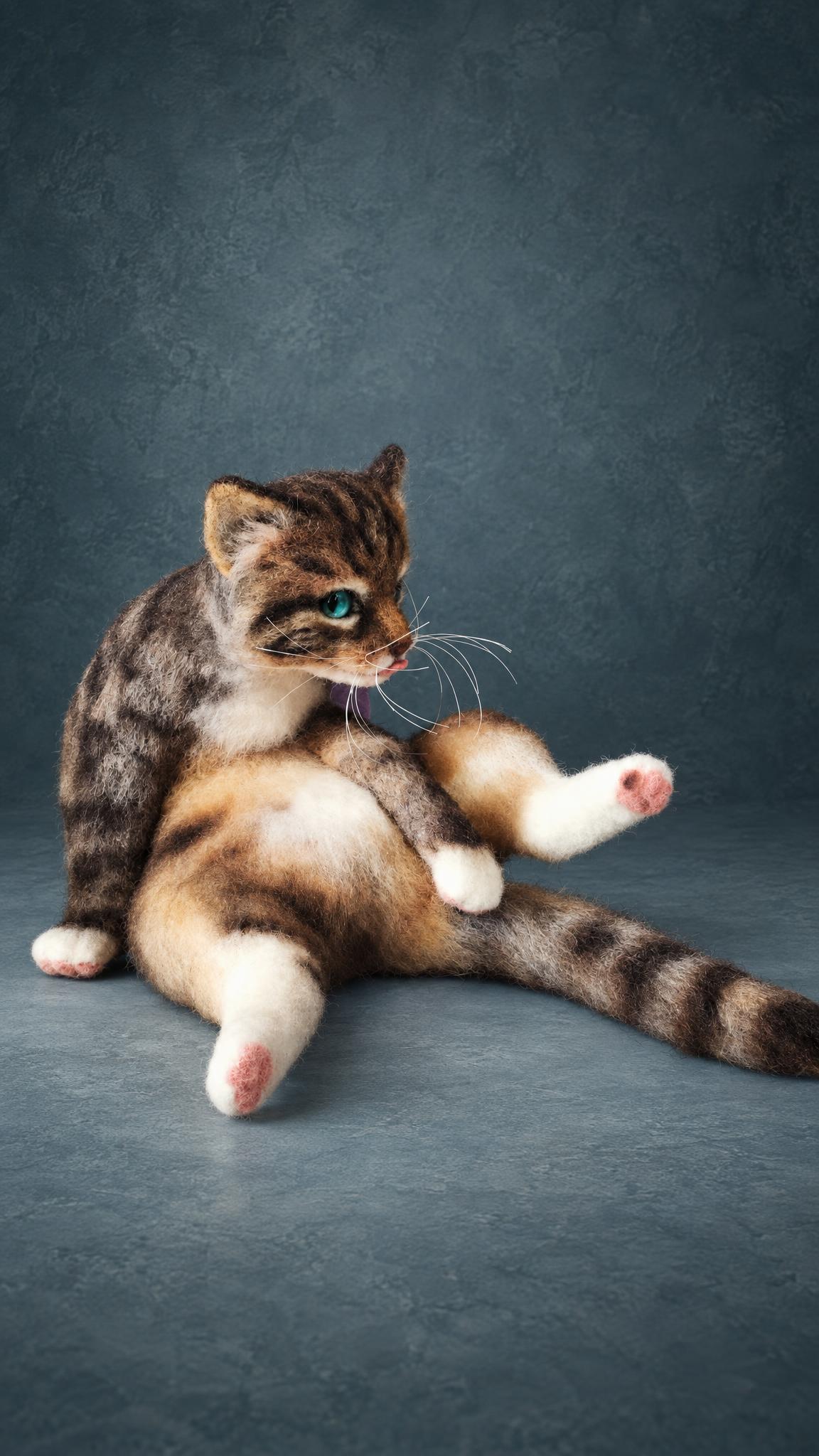 Handmade wool cat licking itself, one hind leg up in the cello pose, custom needle felted tabby