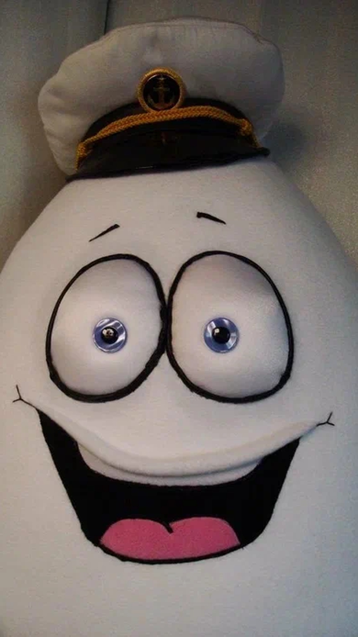 Mr. Egg plush toy face with stitched round eyes, a pink-tongued grin and a gold-anchor captain cap, handmade