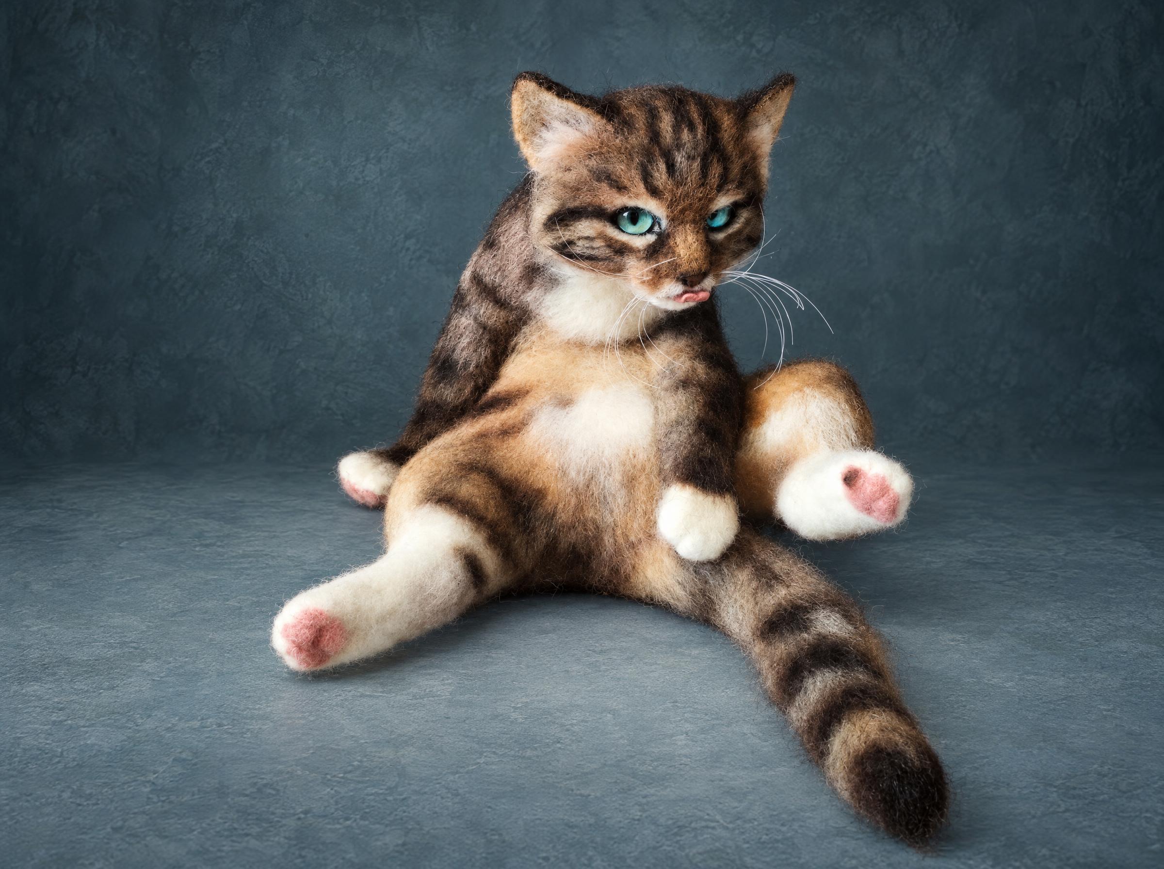 Needle felted tabby cat with its tongue out, legs splayed mid-groom, handmade to order from wool
