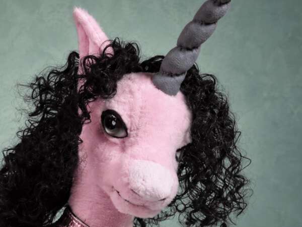 Handmade pink unicorn plush face with a glossy dark eye, a grey spiral horn and a mane of black curls