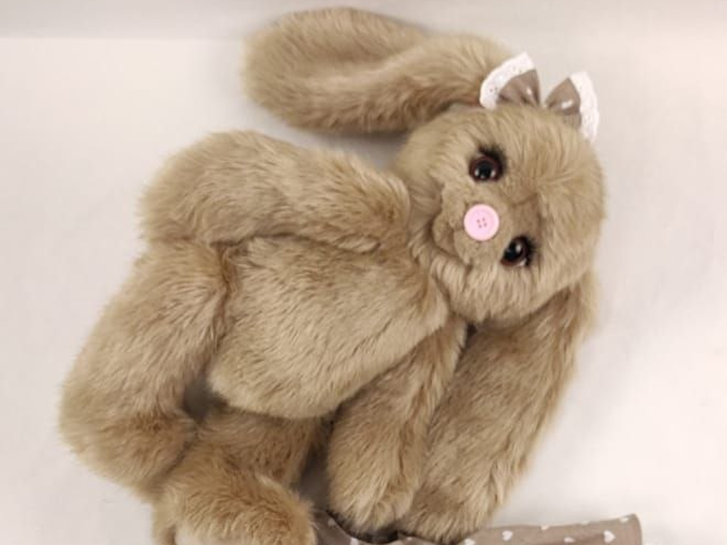 Teddy-style bunny plush sample lying curled up Teddy-style bunny plush sample lying curled up, soft fawn faux fur, pink button nose and a small bow, sewn to order