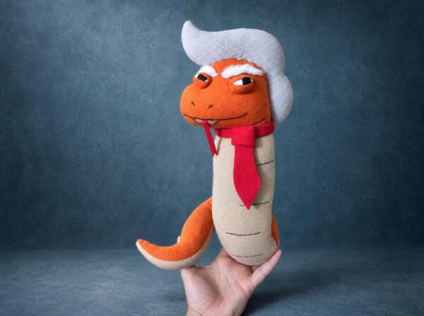 Trump snake plush: orange fleece snake with a white sweep of hair, thick white brows and a red tie, a parody toy sewn to order