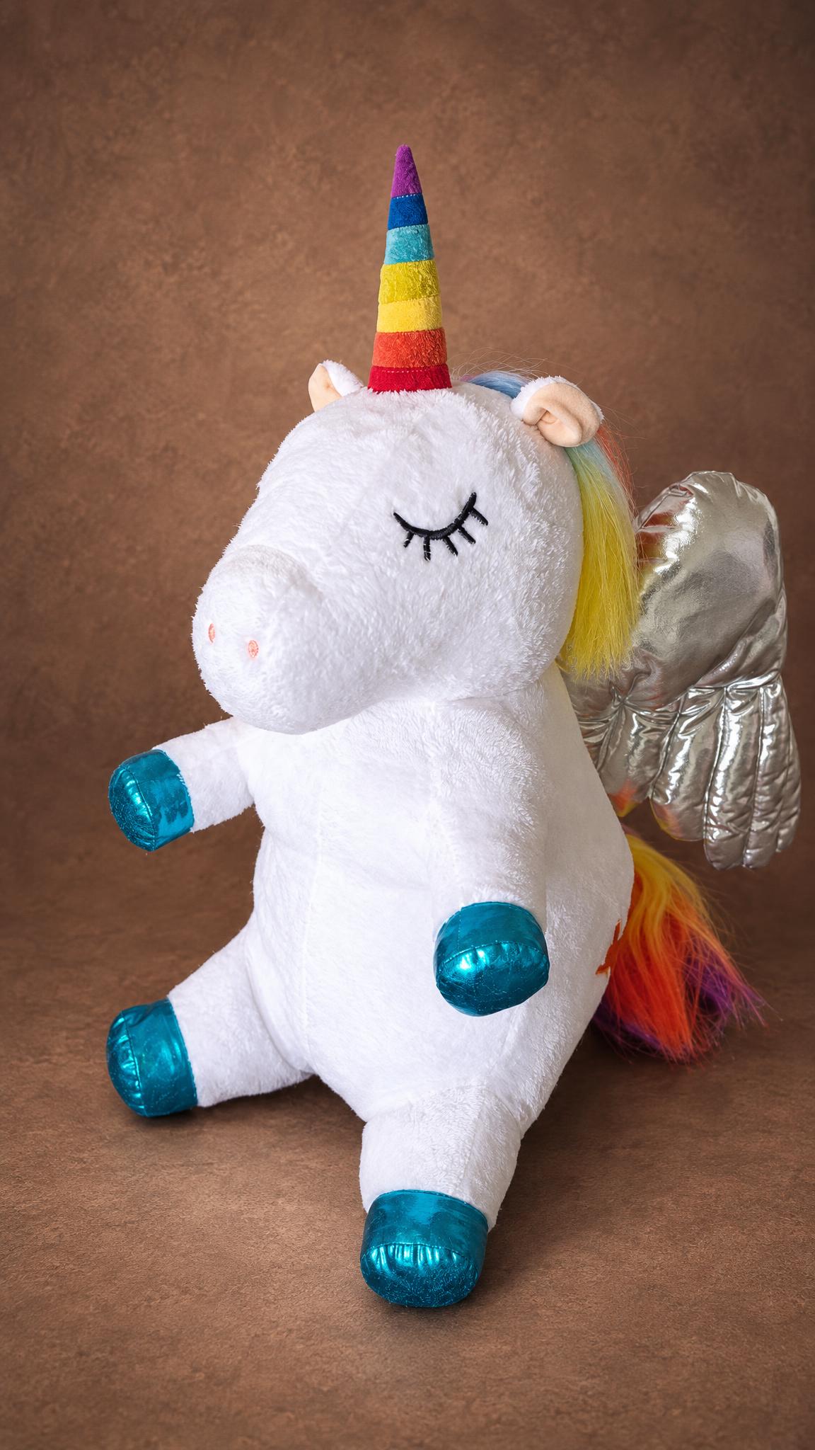 Unicorn stuffed animal from a drawing, sitting with a rainbow-striped horn and shiny teal hooves, made to order