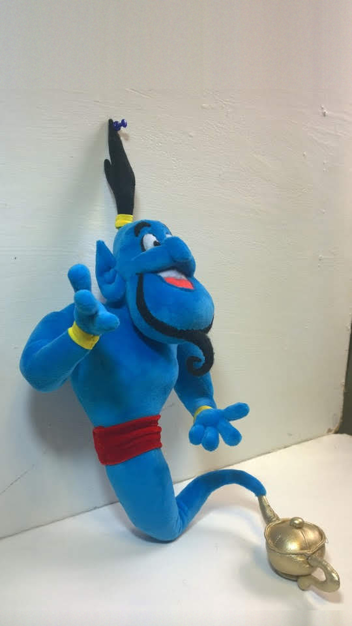 Genie plush from Aladdin with one hand raised, blue body, yellow cuffs, red sash and a golden lamp, handmade