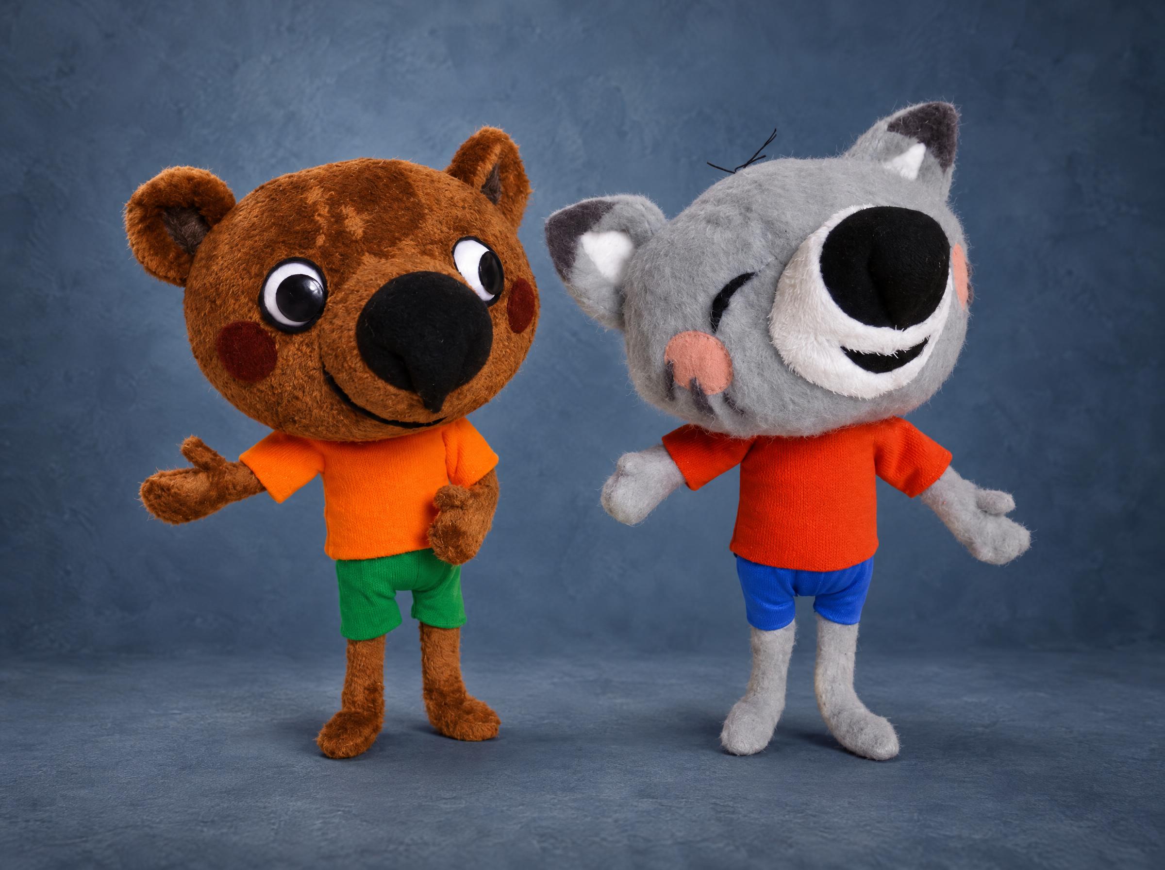 Cartoon bear plush in an orange T-shirt and green shorts beside a grey cat plush in blue shorts, made to order