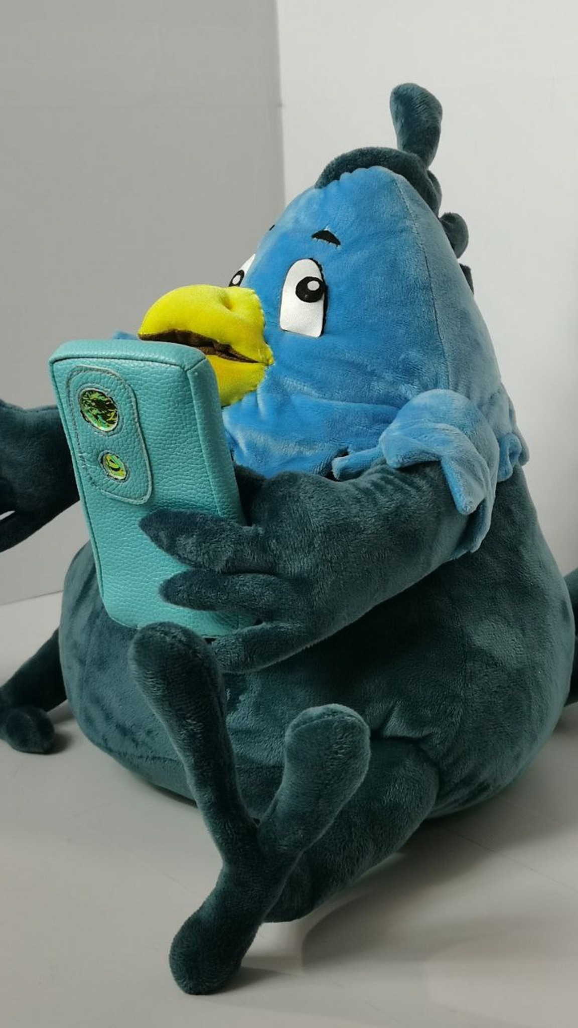Bird mascot plush holding a turquoise phone close to its yellow beak, sitting with legs folded, made to order
