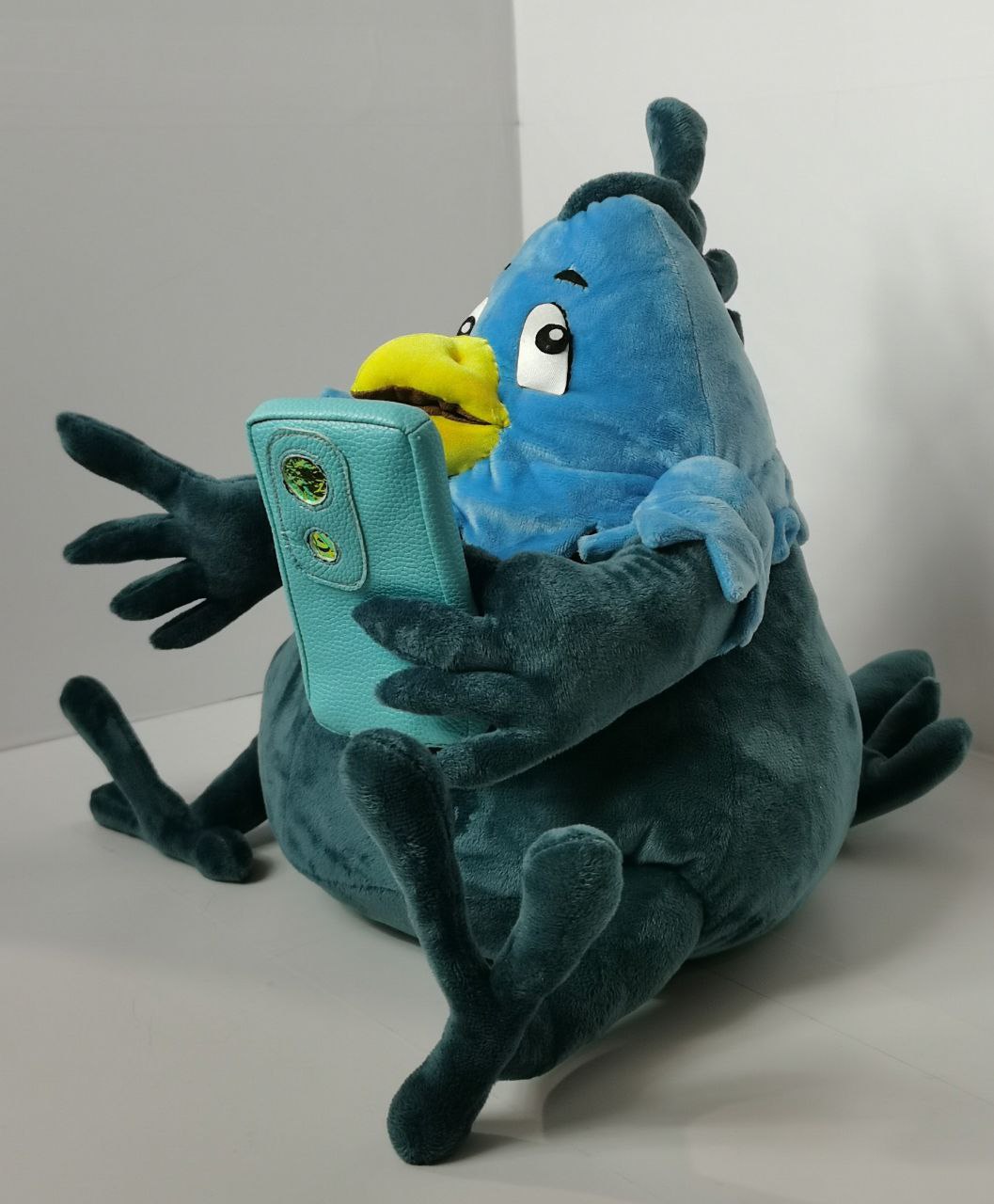 Bird mascot plush with a phone Bird mascot plush holding a turquoise phone close to its yellow beak, sitting with legs folded, made to order