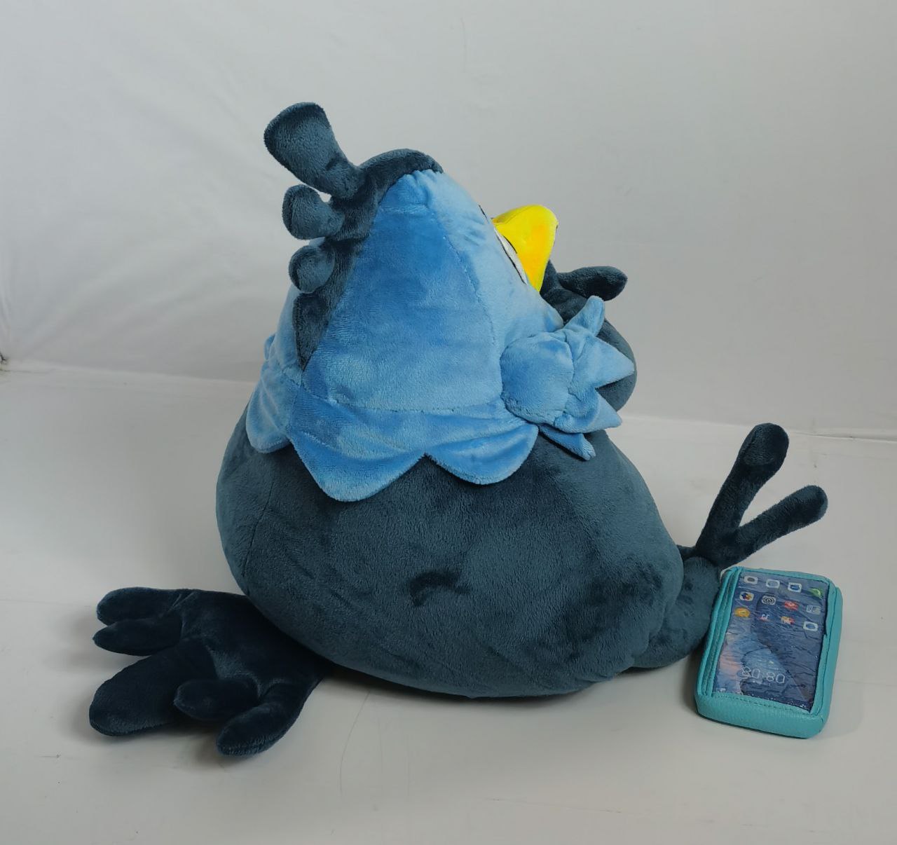 Bird mascot plush with a round body Bird mascot plush with a round dark teal body, long toes and its phone prop beside it, custom sewn to order