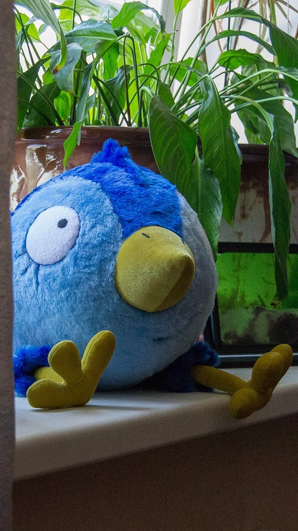 Blue bird plush peeking out from behind a curtain, a handmade prototype of an artist's character