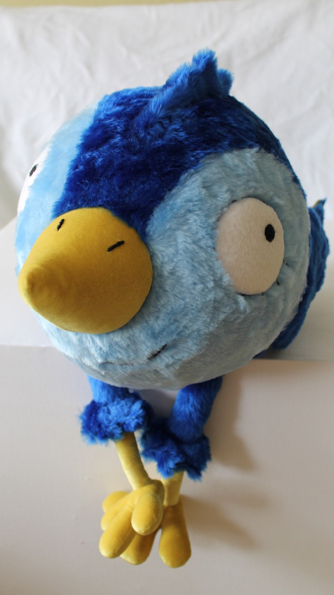 Round blue bird plush with long yellow legs dangling from a shelf, a custom prototype made to order