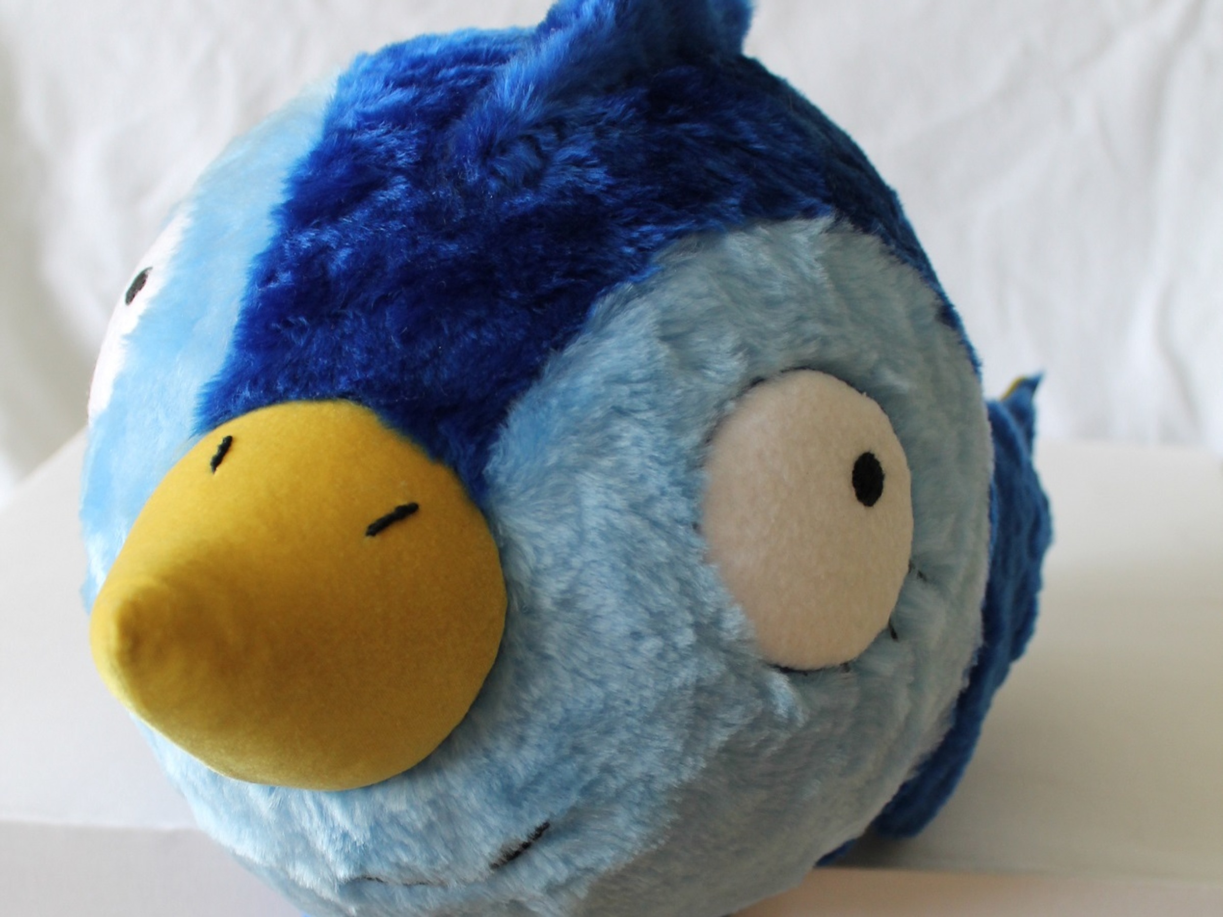 Blue bird plush prototype with a yellow beak and big white eyes, handmade to order from an artist's drawing
