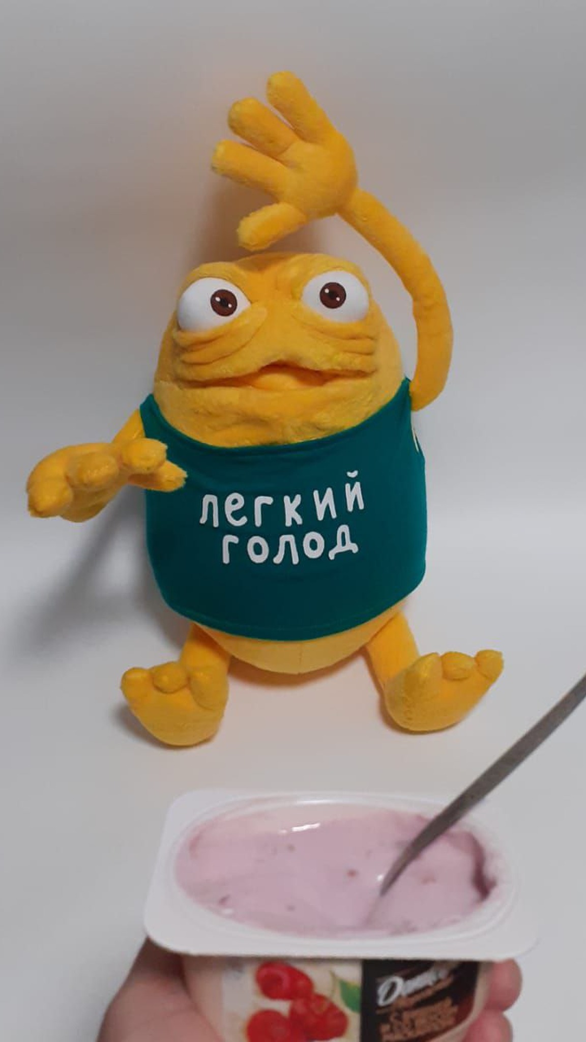 Yellow TV ad monster plush with one arm raised over a yogurt cup, a custom mascot plush sewn by hand
