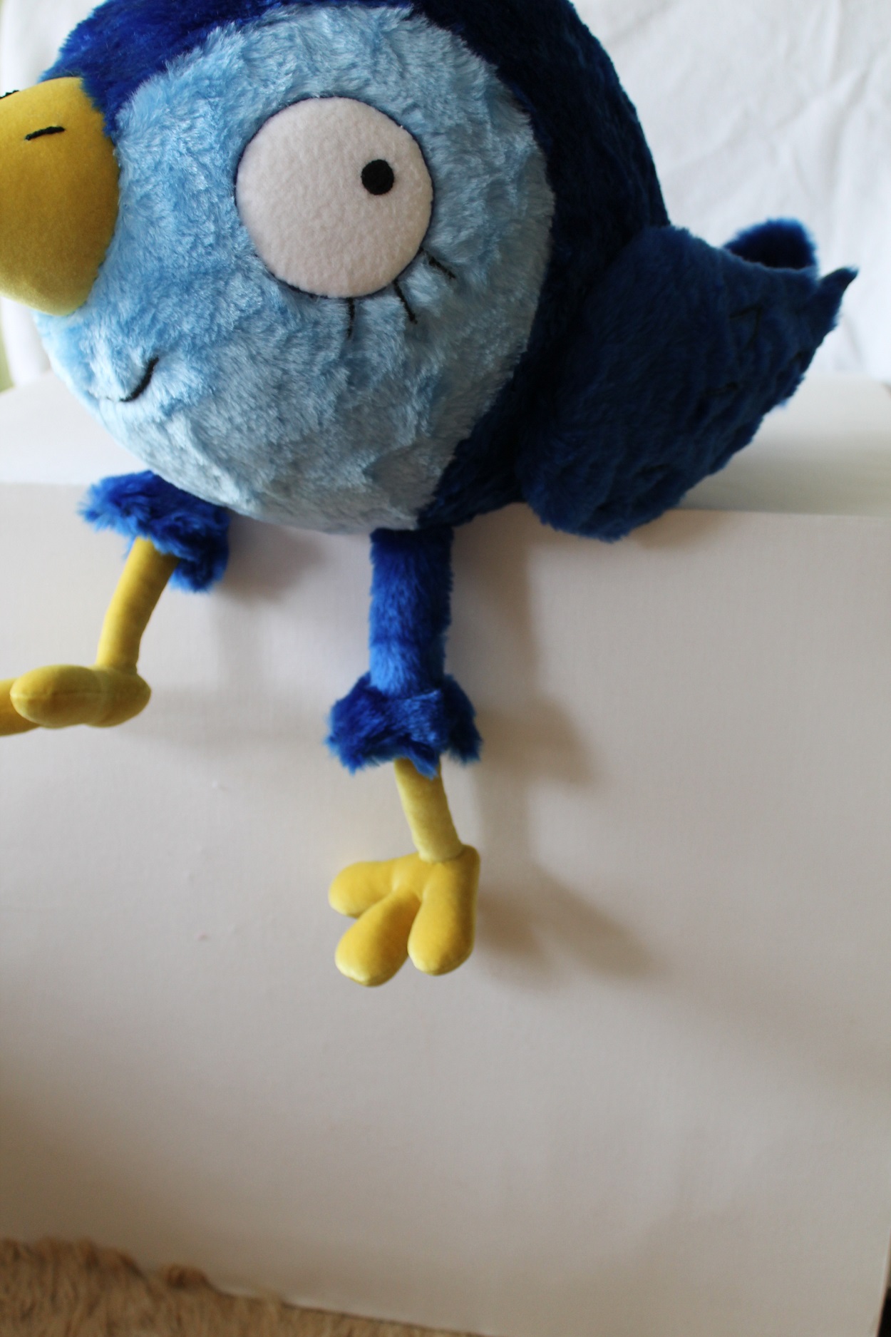 Custom blue bird plush with yellow legs Custom blue bird plush sitting on a ledge with its yellow legs hanging down, embroidered lashes and smile