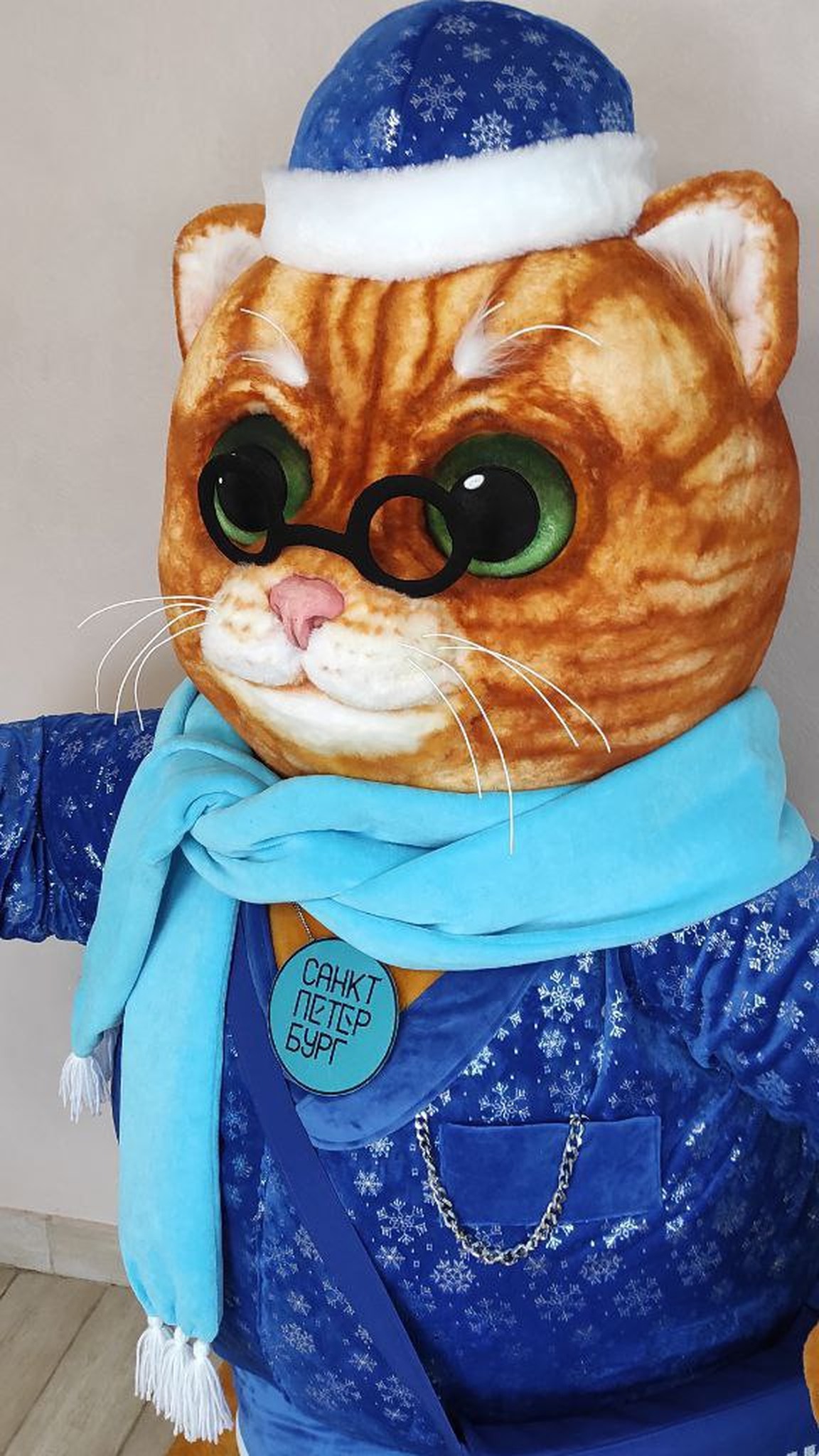 Custom cat mascot plush in glasses, a blue hat with white faux fur trim and a light-blue scarf, sewn to order