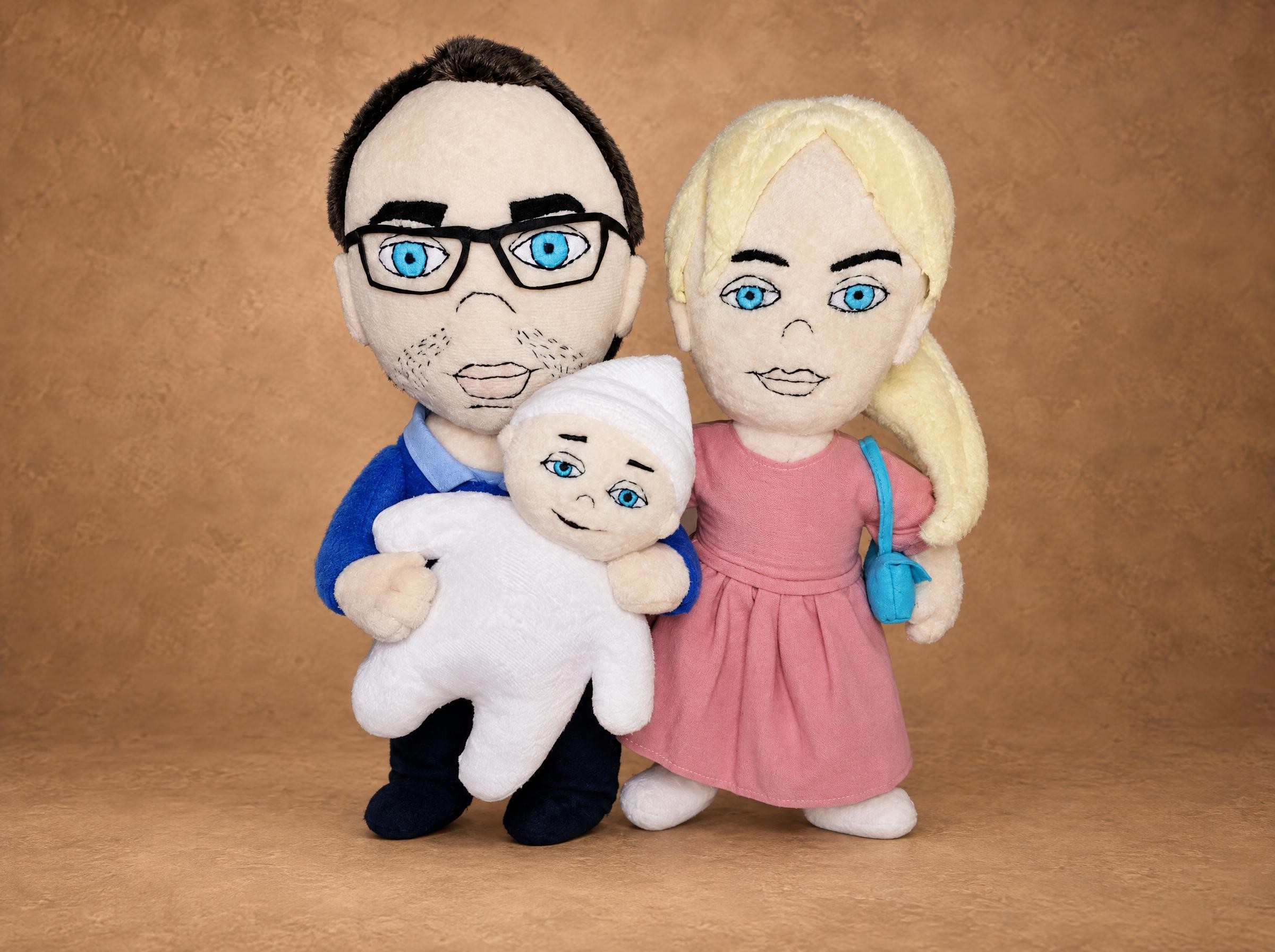 Custom family dolls made to order: dad in glasses holding the baby in a white cap, mom in a pink dress