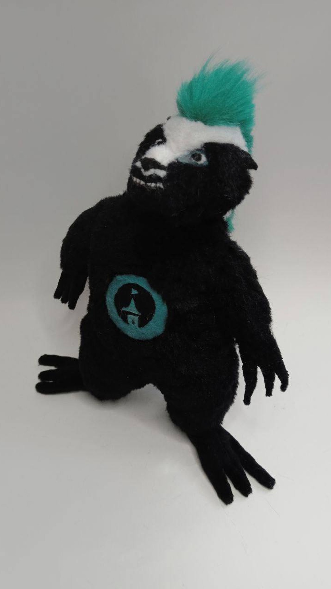 Custom honey badger plush grinning with small white teeth and a teal logo patch, a mascot sewn to order
