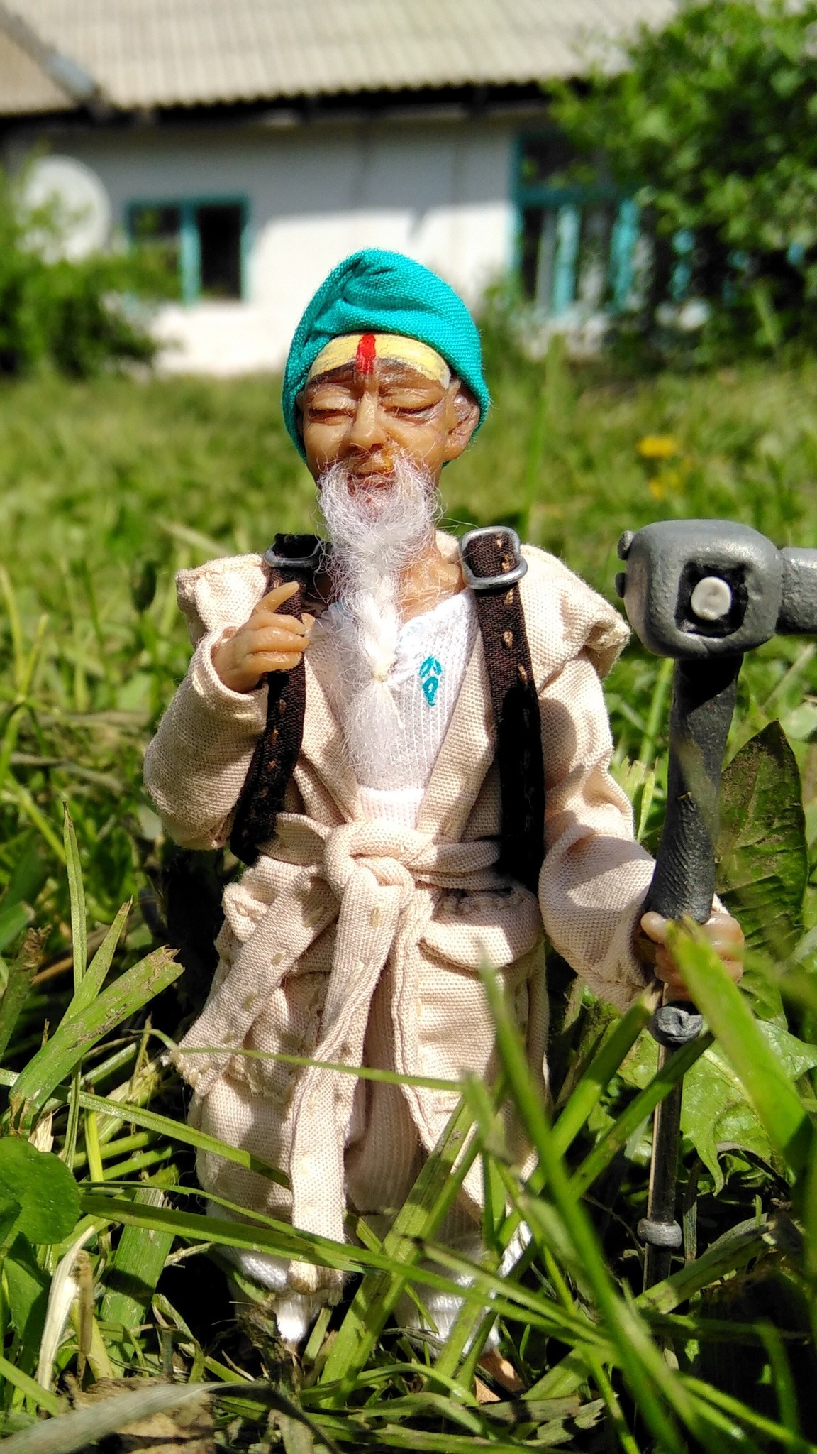 Bearded traveler mascot doll in a turquoise turban and cream coat in the grass, handmade to order for a brand