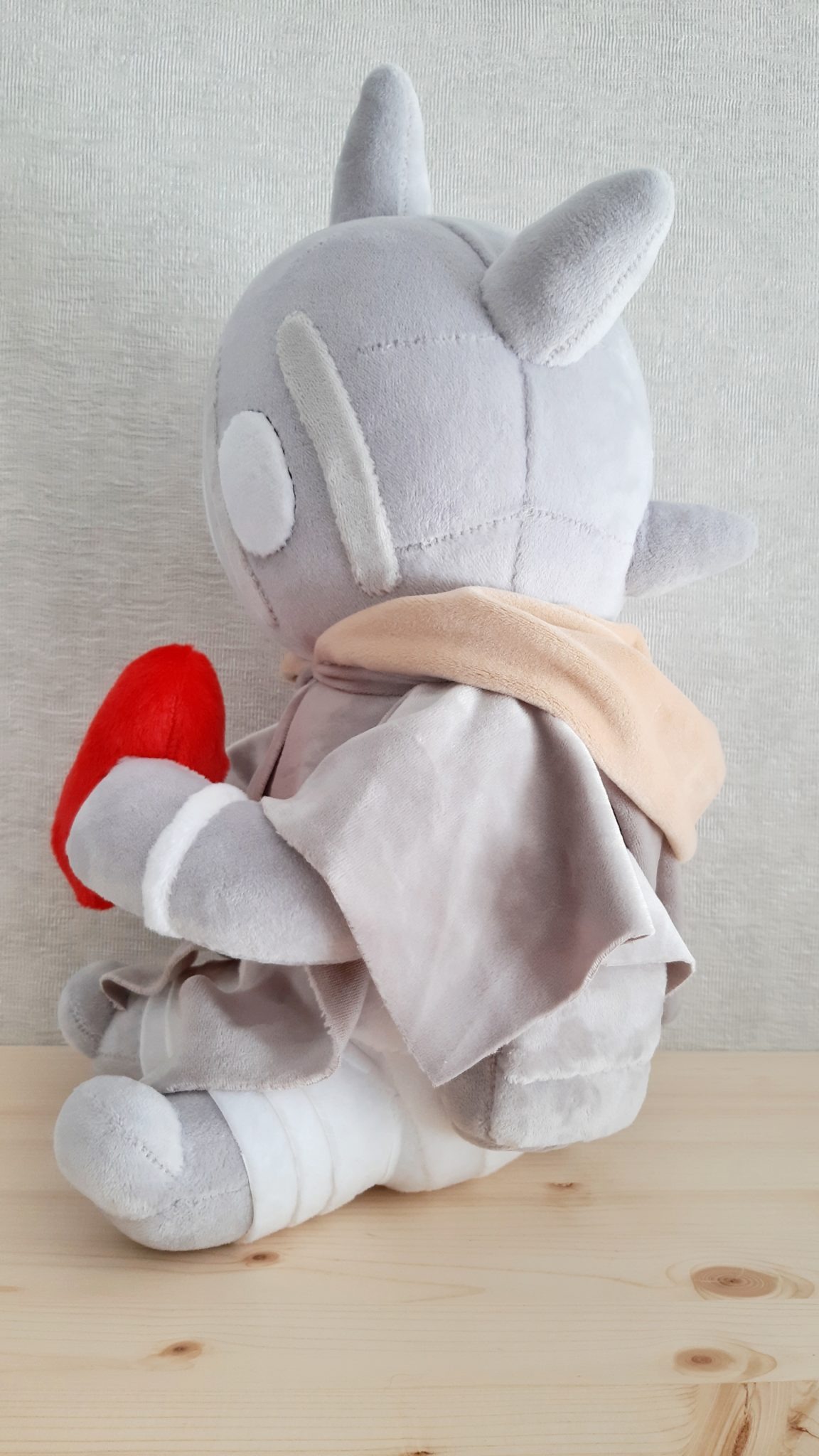 Custom monster plush with a peach scarf and grey cloak, red heart in its paws, legs wrapped in white bands