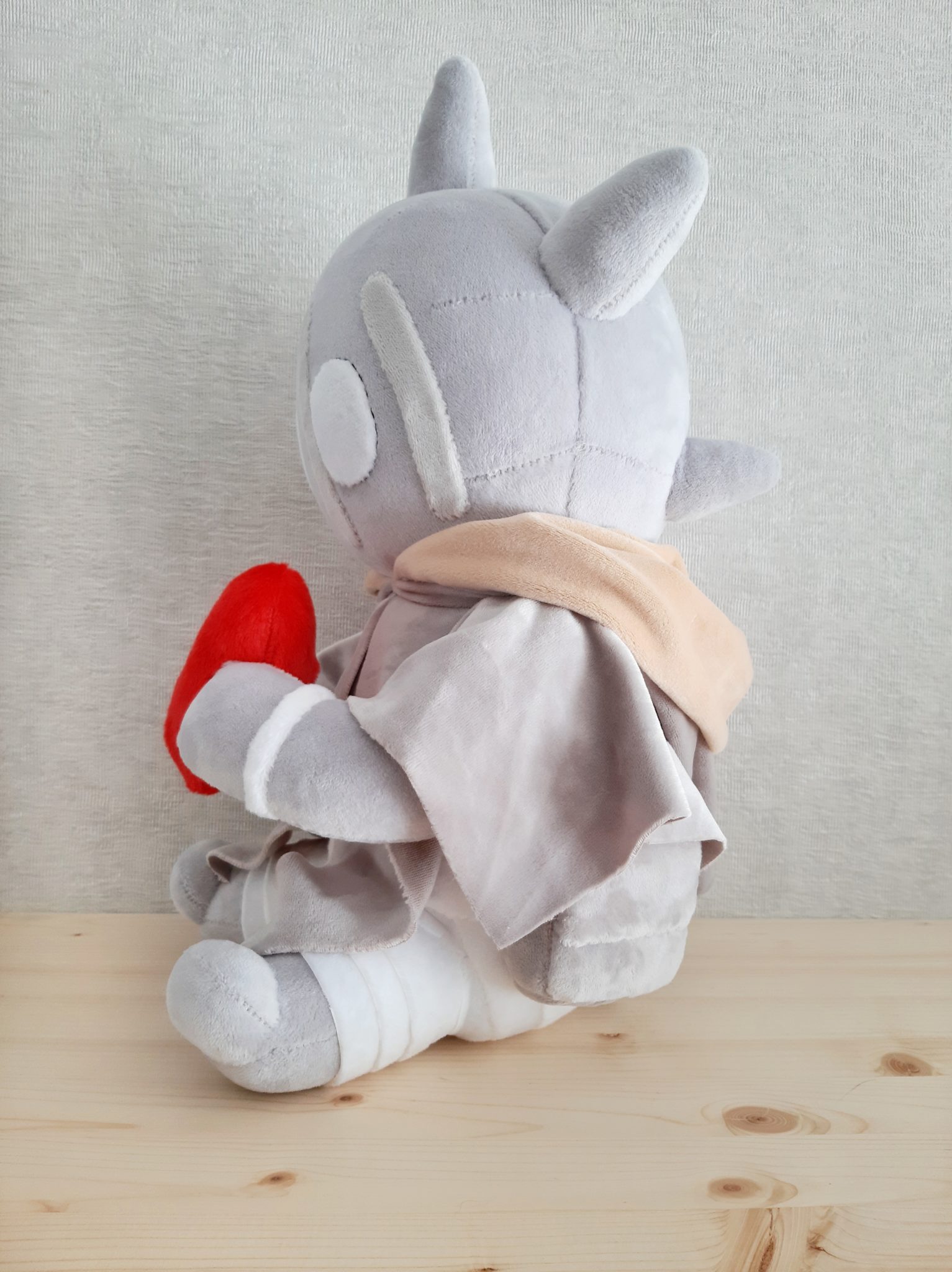 Custom monster plush in a scarf and cloak Custom monster plush with a peach scarf and grey cloak, red heart in its paws, legs wrapped in white bands