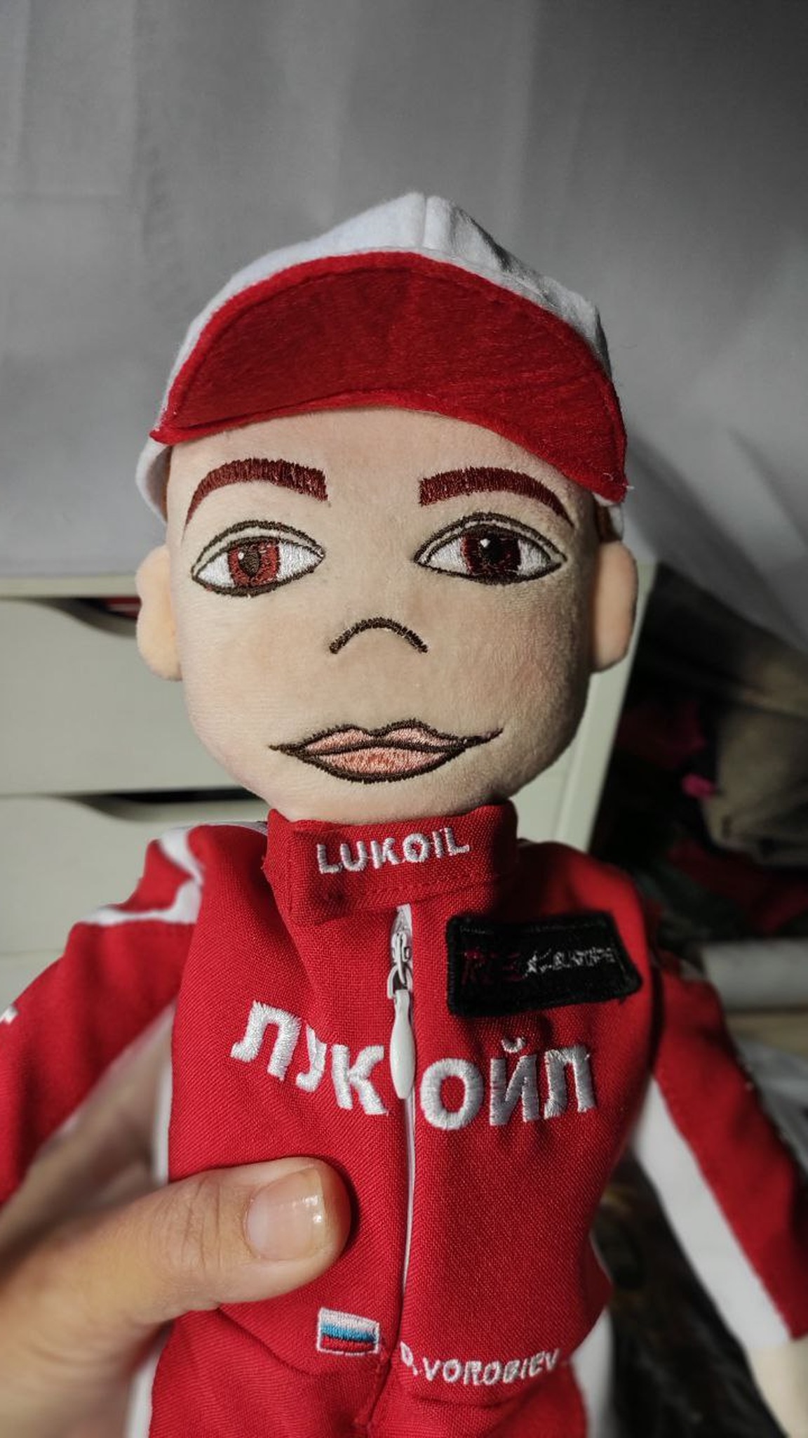 Custom plush doll with an embroidered face, red cap and logo on the racing suit collar, handmade to order