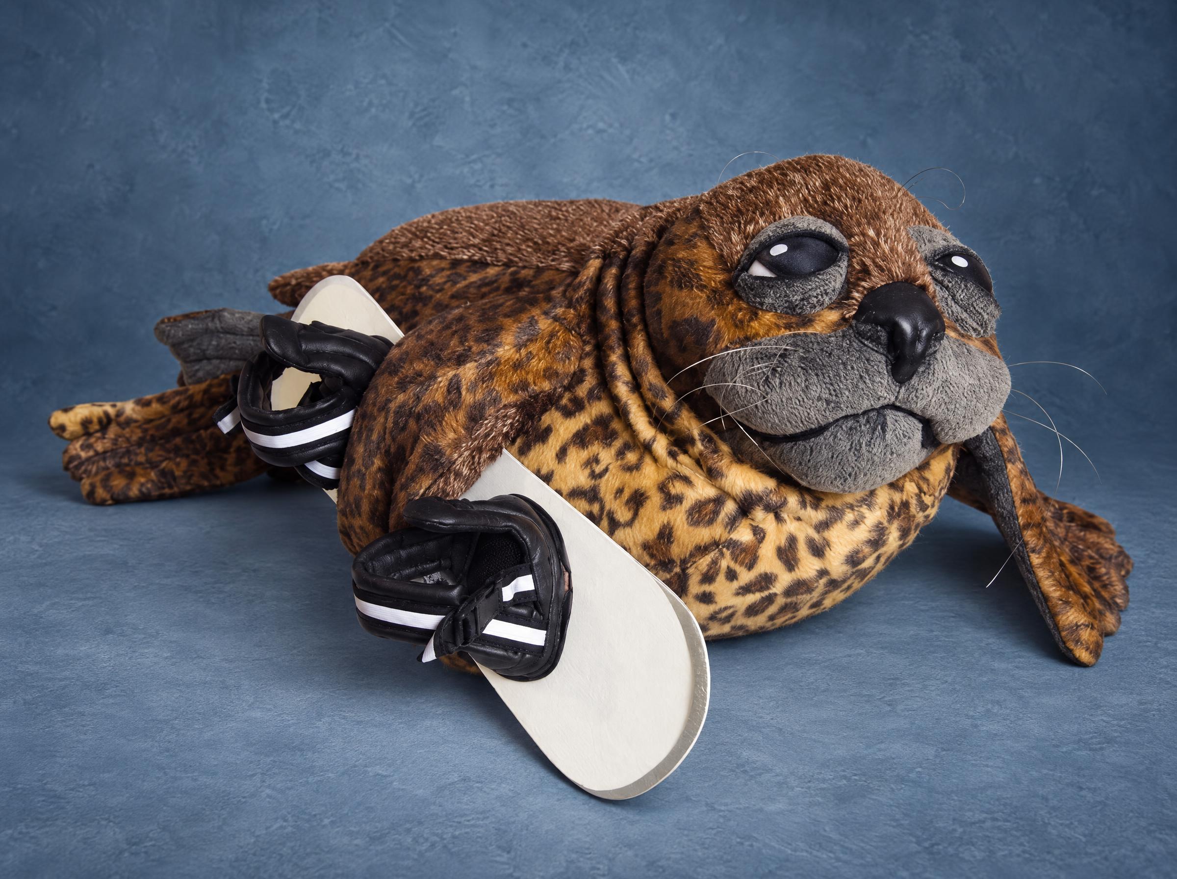 Custom seal plush made to order: spotted golden faux fur, grey whiskered muzzle, hugging a white snowboard