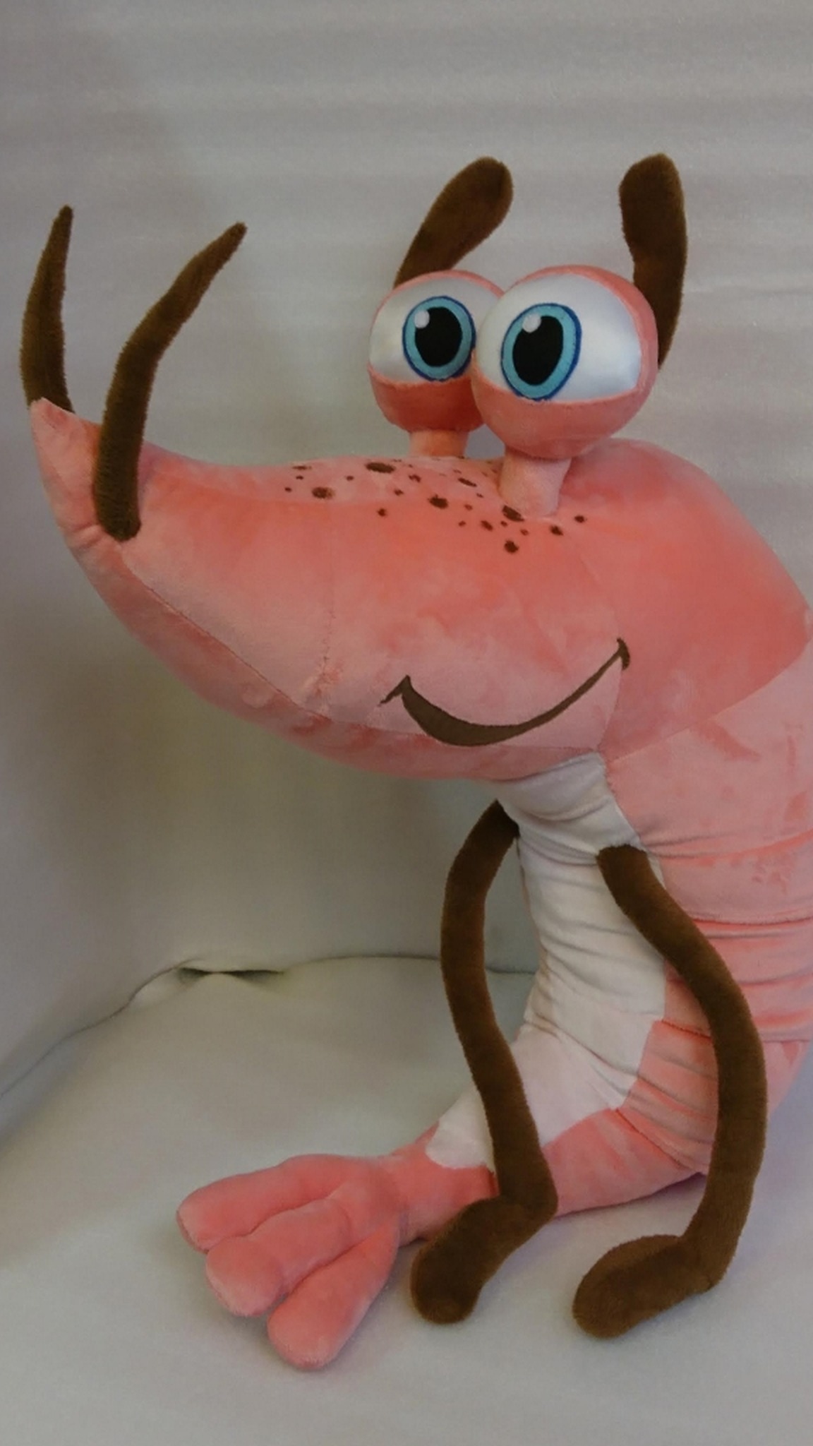 Custom shrimp mascot plush with freckles on its long pink head and thin brown legs, sewn to order for a company