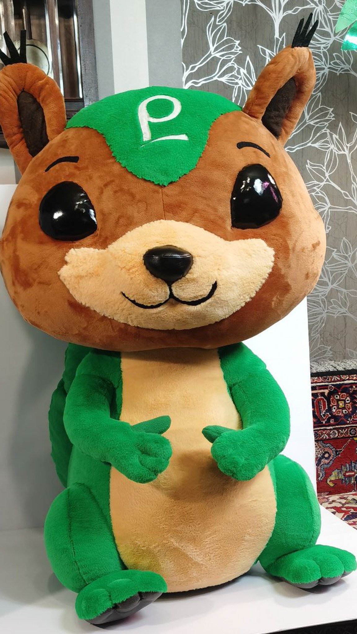 Custom squirrel mascot plush with the company logo on its forehead and green paws, made to order