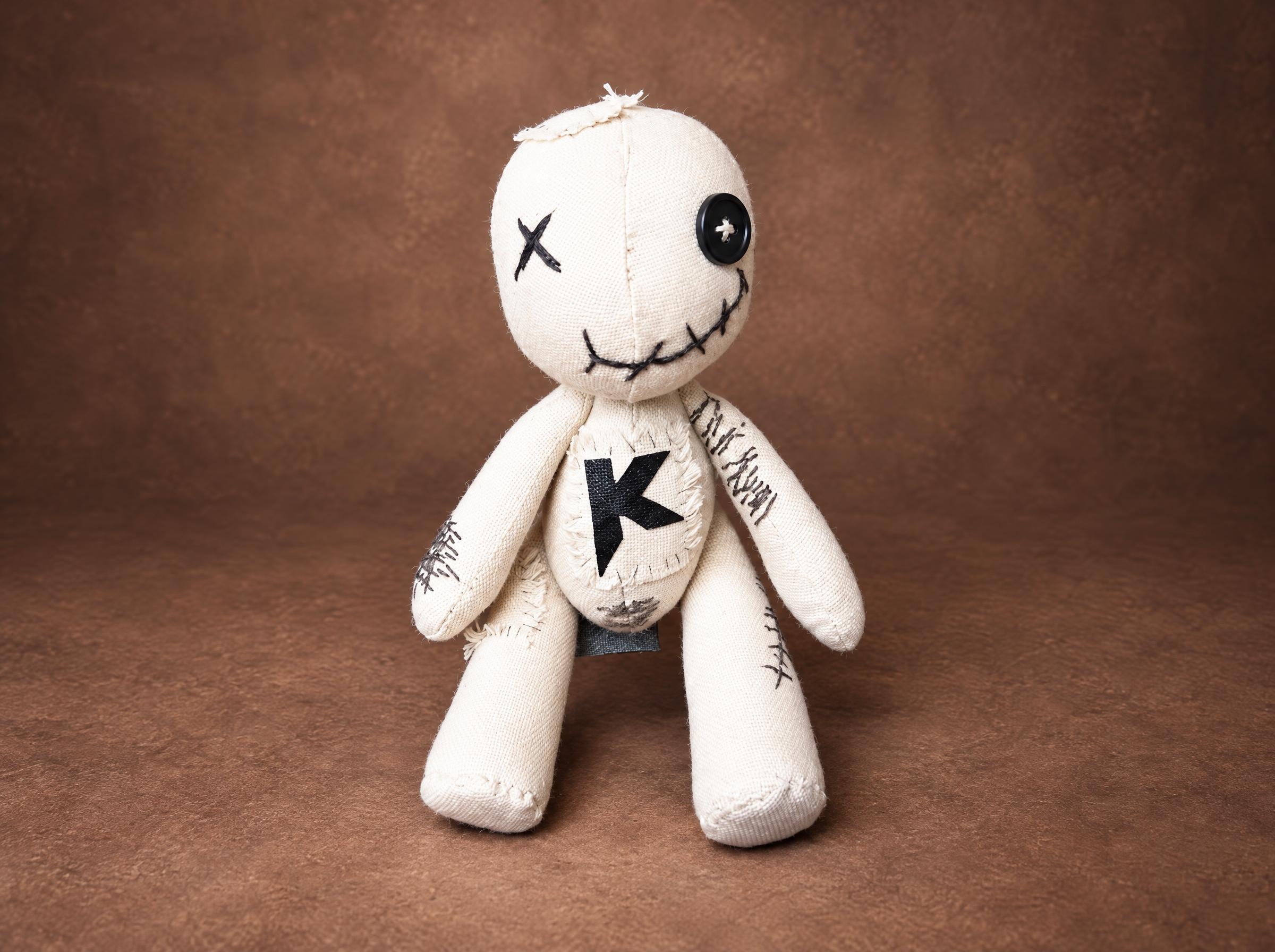 Custom voodoo doll in cream canvas with a button eye, stitched grin and a black K patch, handmade to order