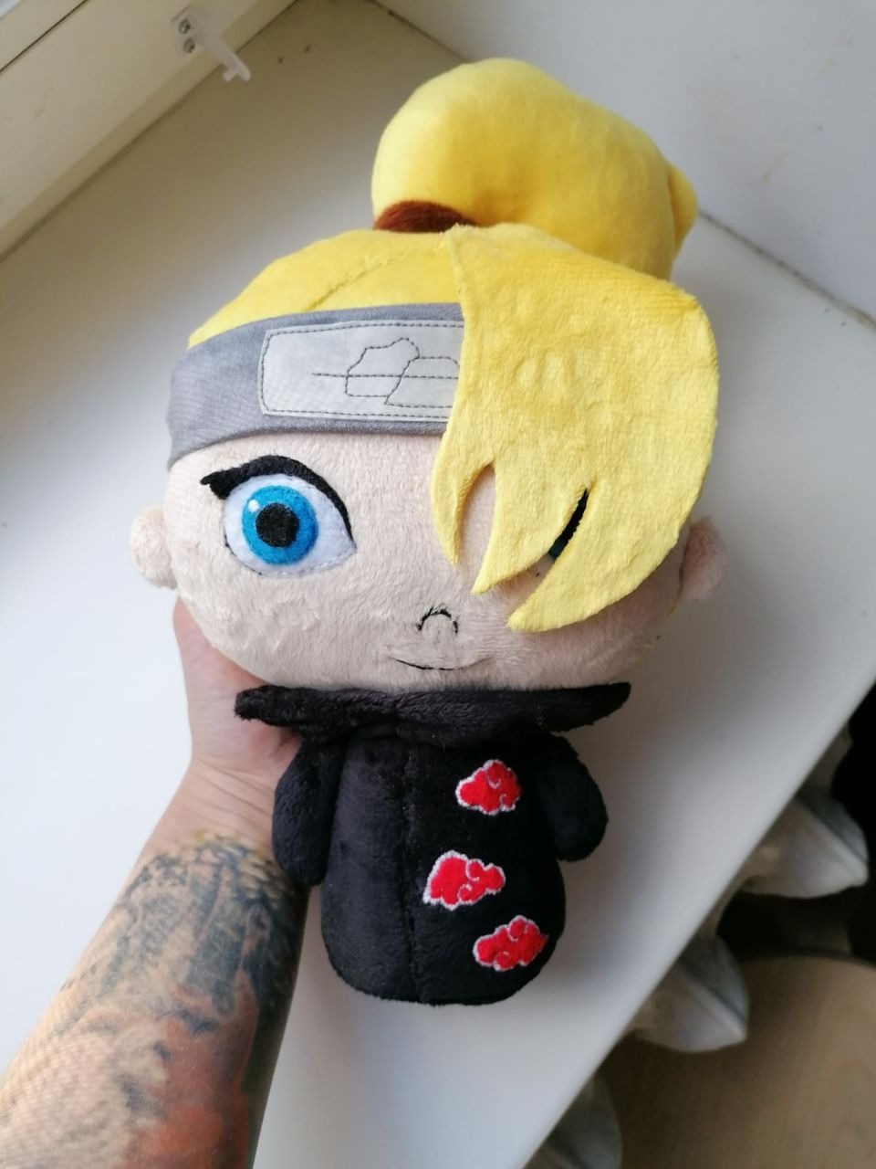 Deidara plush with a blue eye and Akatsuki clouds Deidara plush held in one hand: big blue eye, long yellow bang and embroidered Akatsuki clouds, custom made