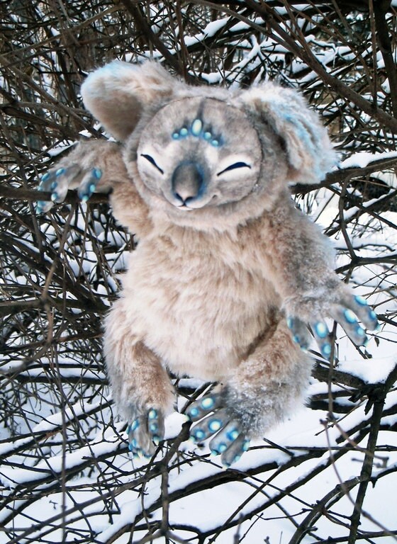 Koala plush in snowy branches Handmade koala plush with long arms and turquoise-spotted paws hanging in snowy branches