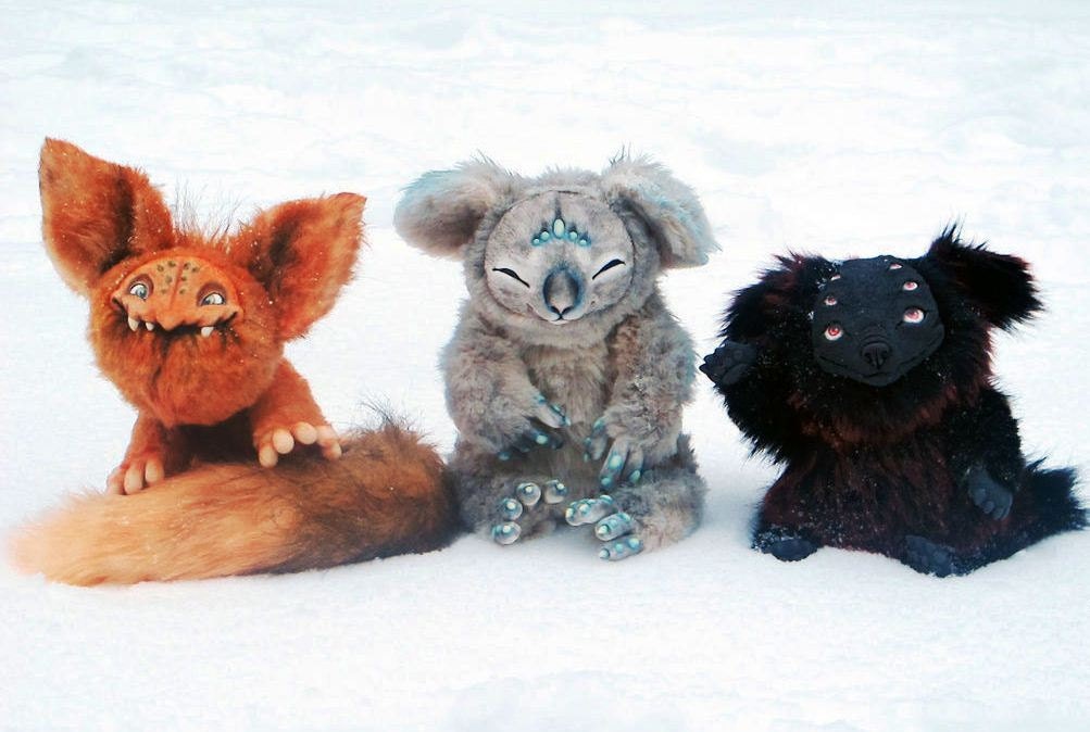 Fantasy koala plush with two creature friends Fantasy koala plush sitting in the snow between a red big-eared creature and a black four-eyed creature