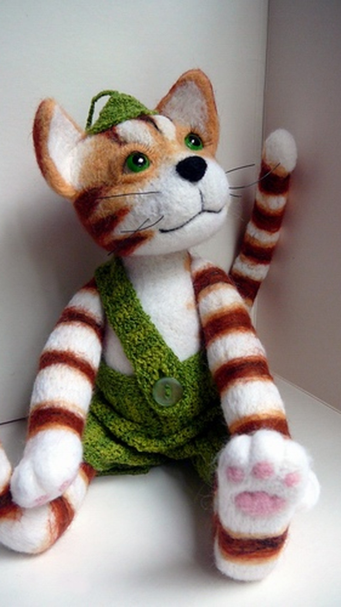 Felted Findus cat toy sitting with pink paw pads and knitted green trousers with a button, handmade to order