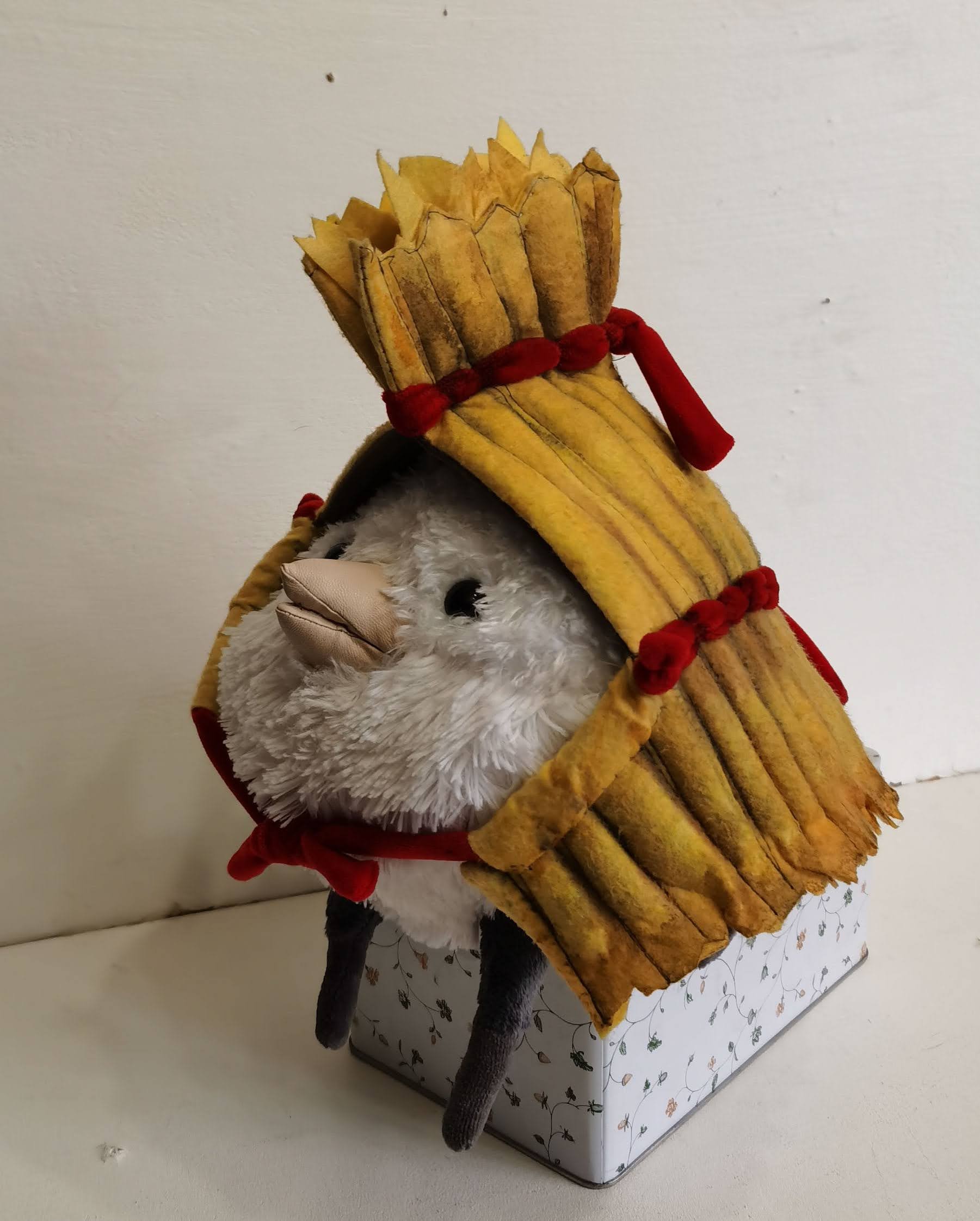 Fluffy bird plush in a straw cape Fluffy bird plush under a ribbed straw cape with a fringed tuft and red velvety bows, sewn by hand to order