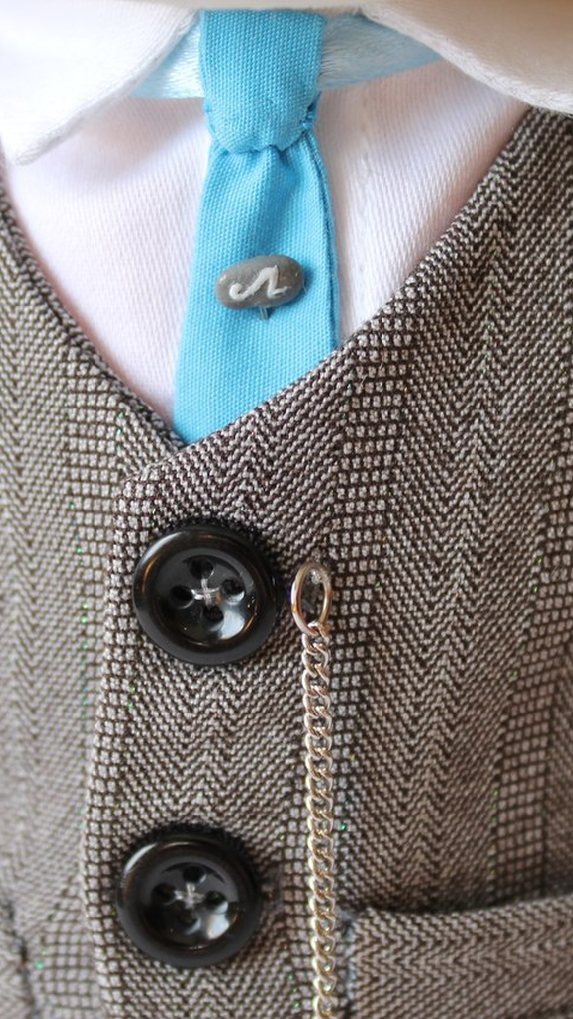 Blue tie with a tie clip and a herringbone vest with black buttons on a handmade fox mascot plush
