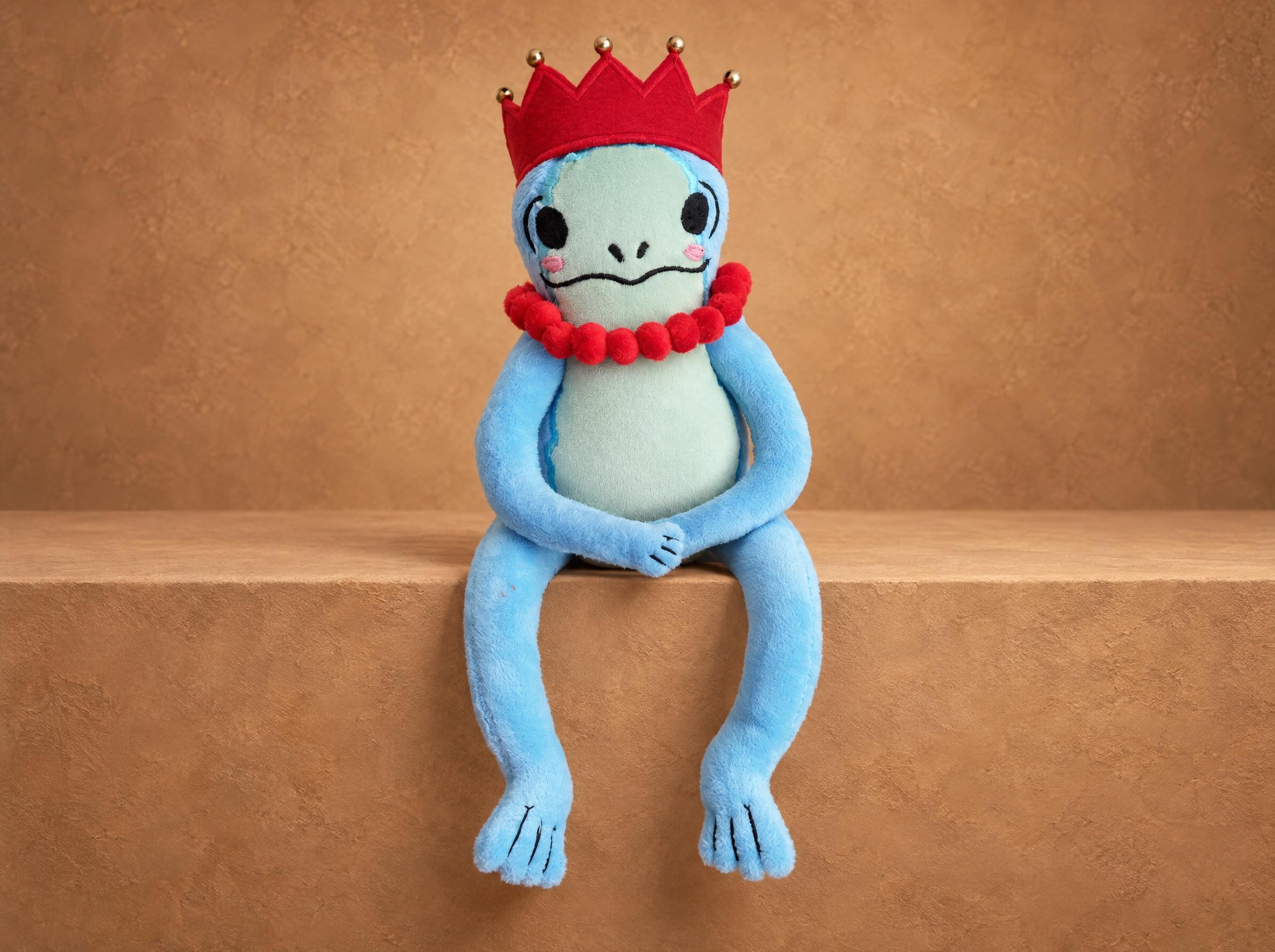 Frog princess plush made to order from a sticker: lanky blue frog in a red crown with a pom-pom necklace