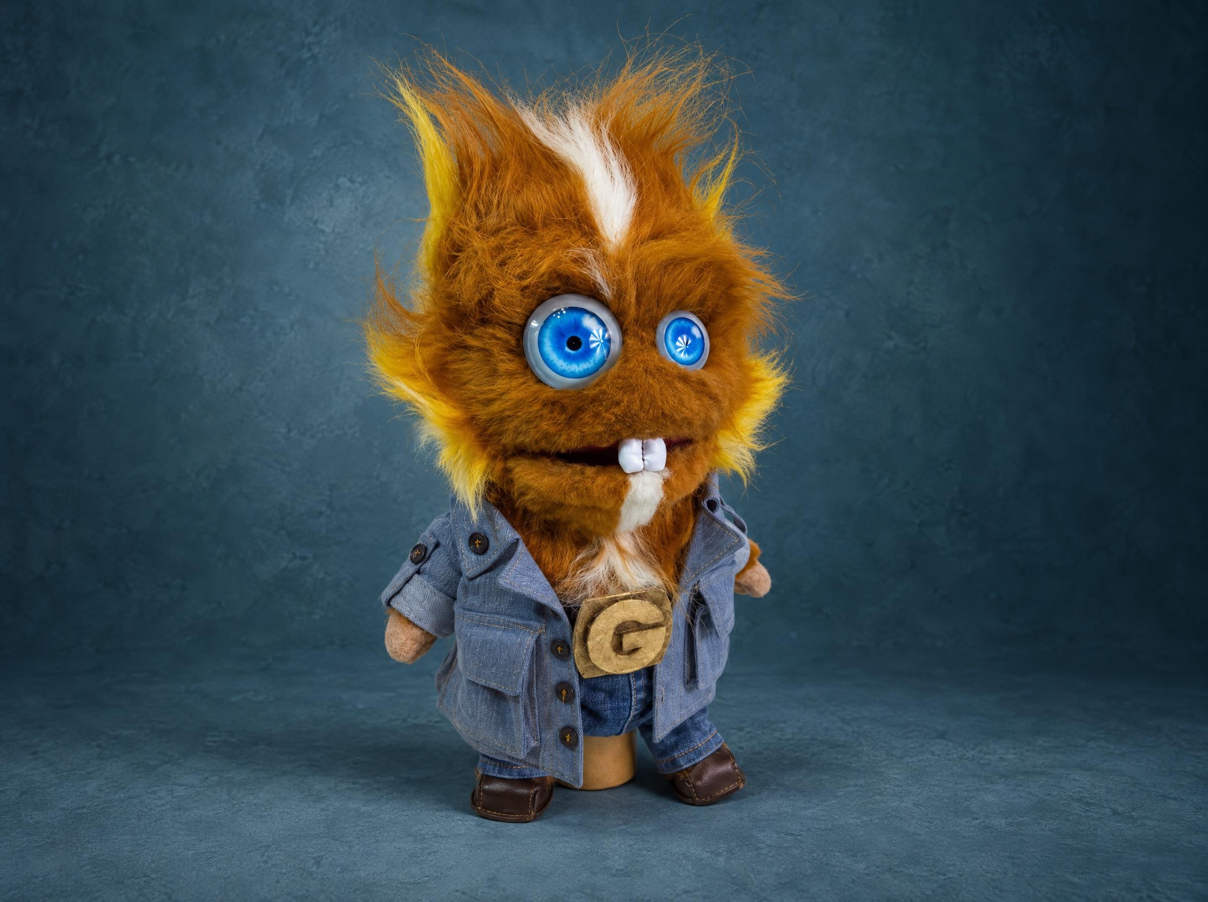 Furry monster puppet with odd blue eyes, buck teeth and a denim jacket with a gold G buckle, made to order
