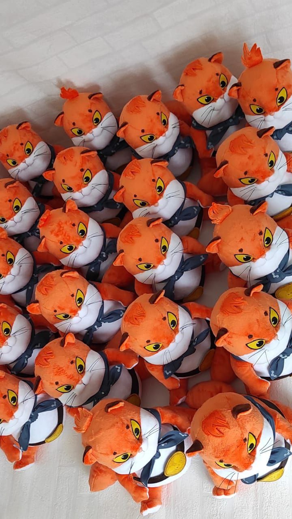 Pile of handmade ginger cat plush from a game merch batch: yellow eyes, blue bandanas, made to order