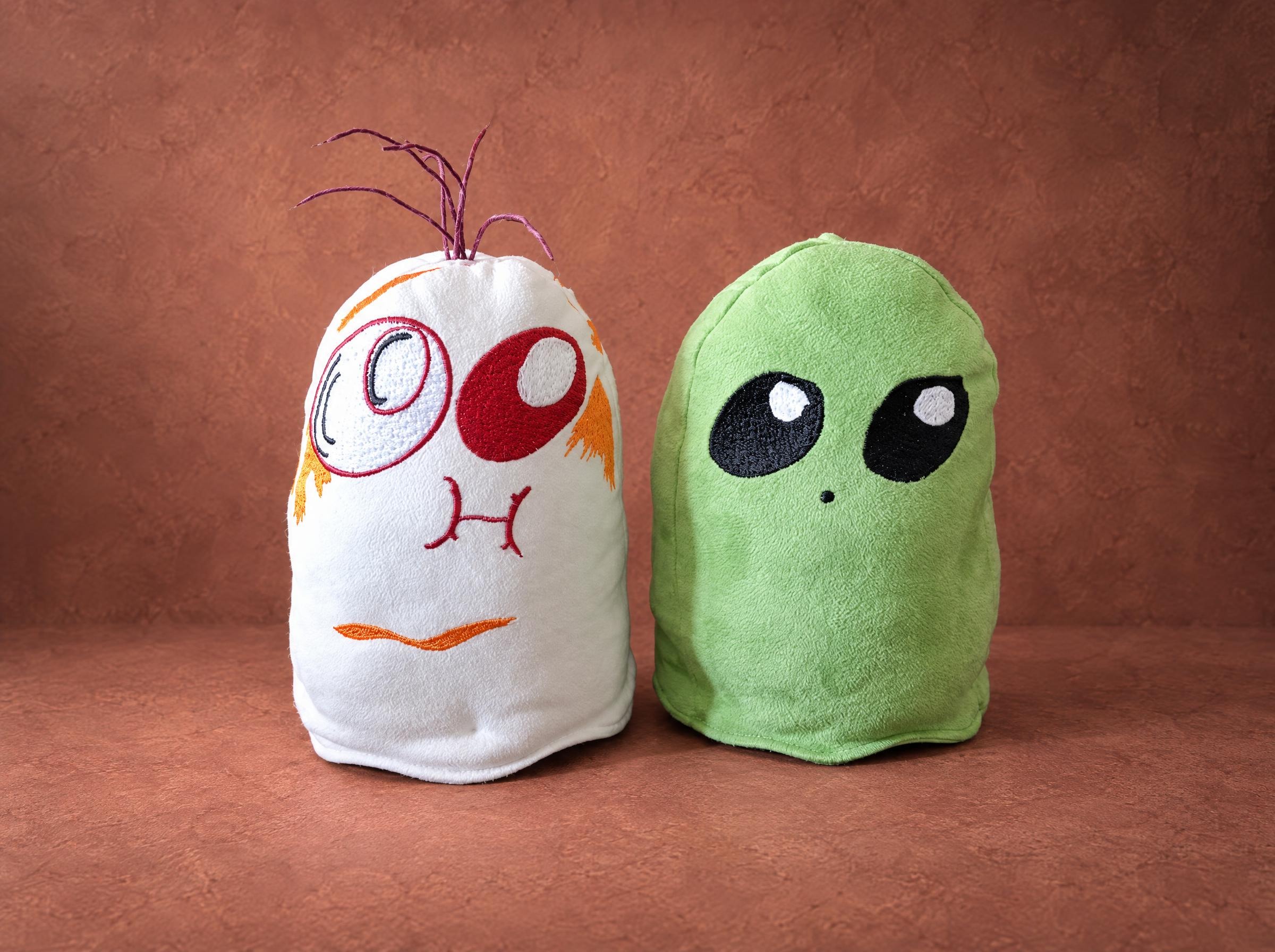 Two ghost plushies sewn by hand from a drawing: a white ghost with a red eye and a green one with alien eyes
