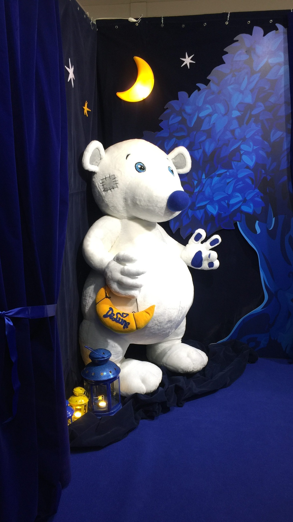 White giant bear mascot plush on a trade show stand under a glowing moon, a brand character sewn to order